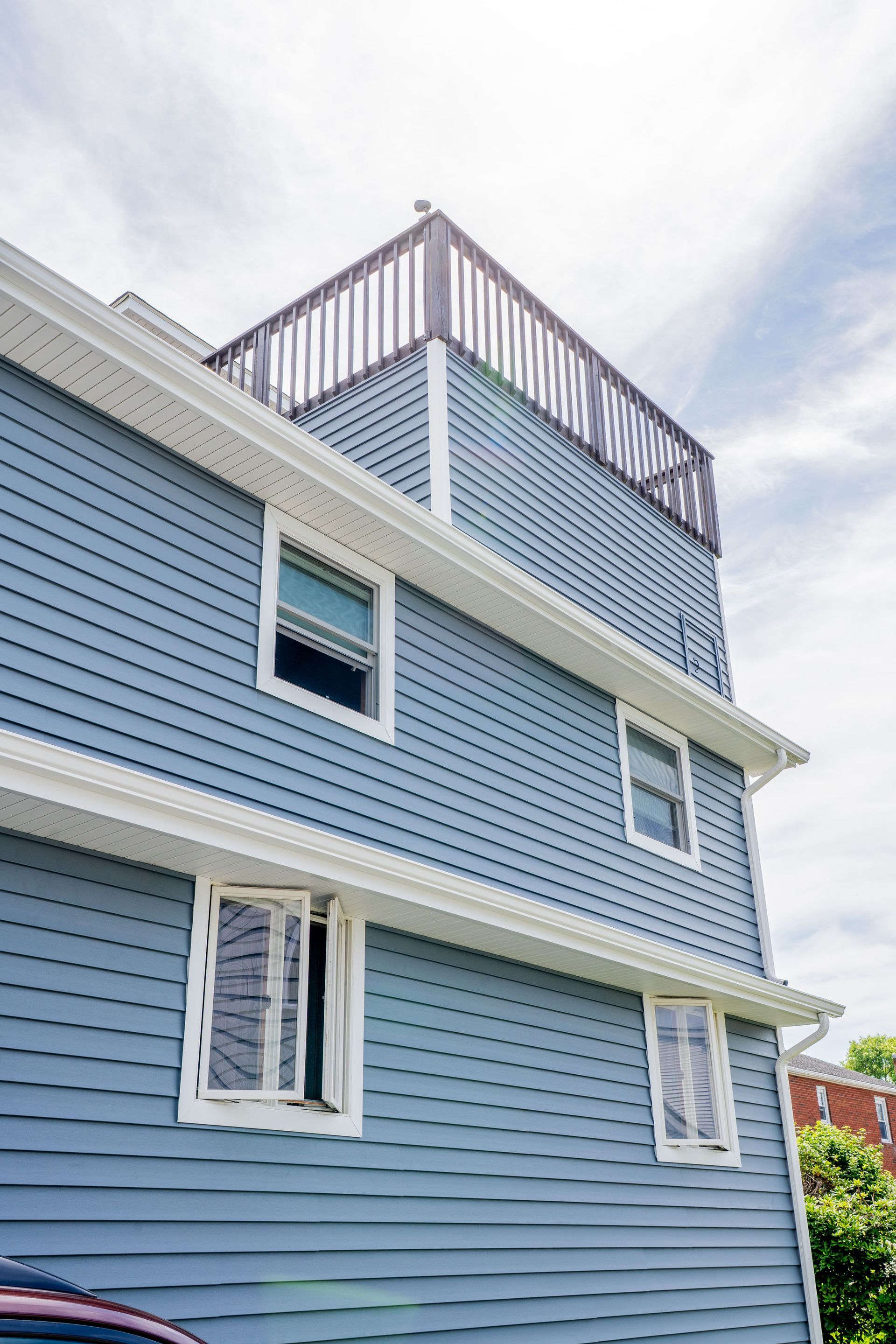 Blue house exterior with white trim and a rooftop deck against a cloudy sky