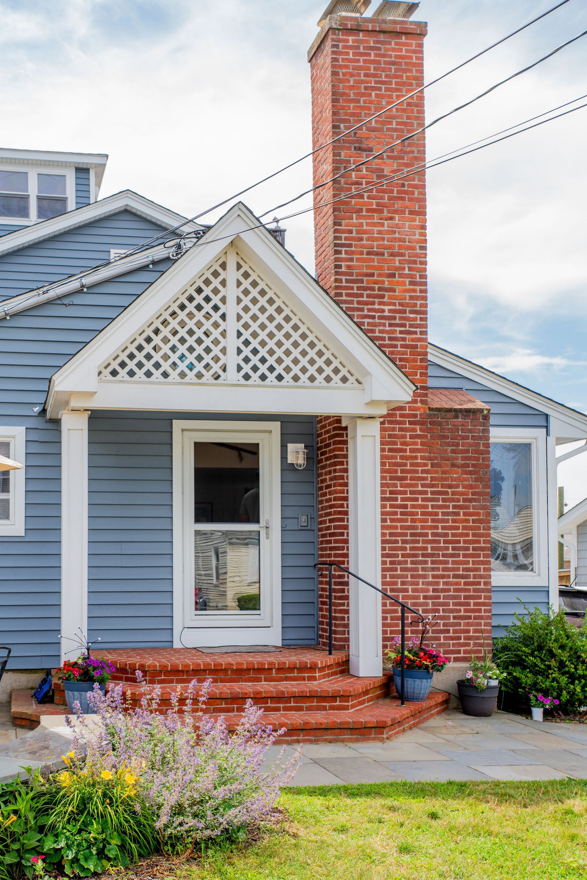 Blue house with brick steps, porch, and tall brick chimney.