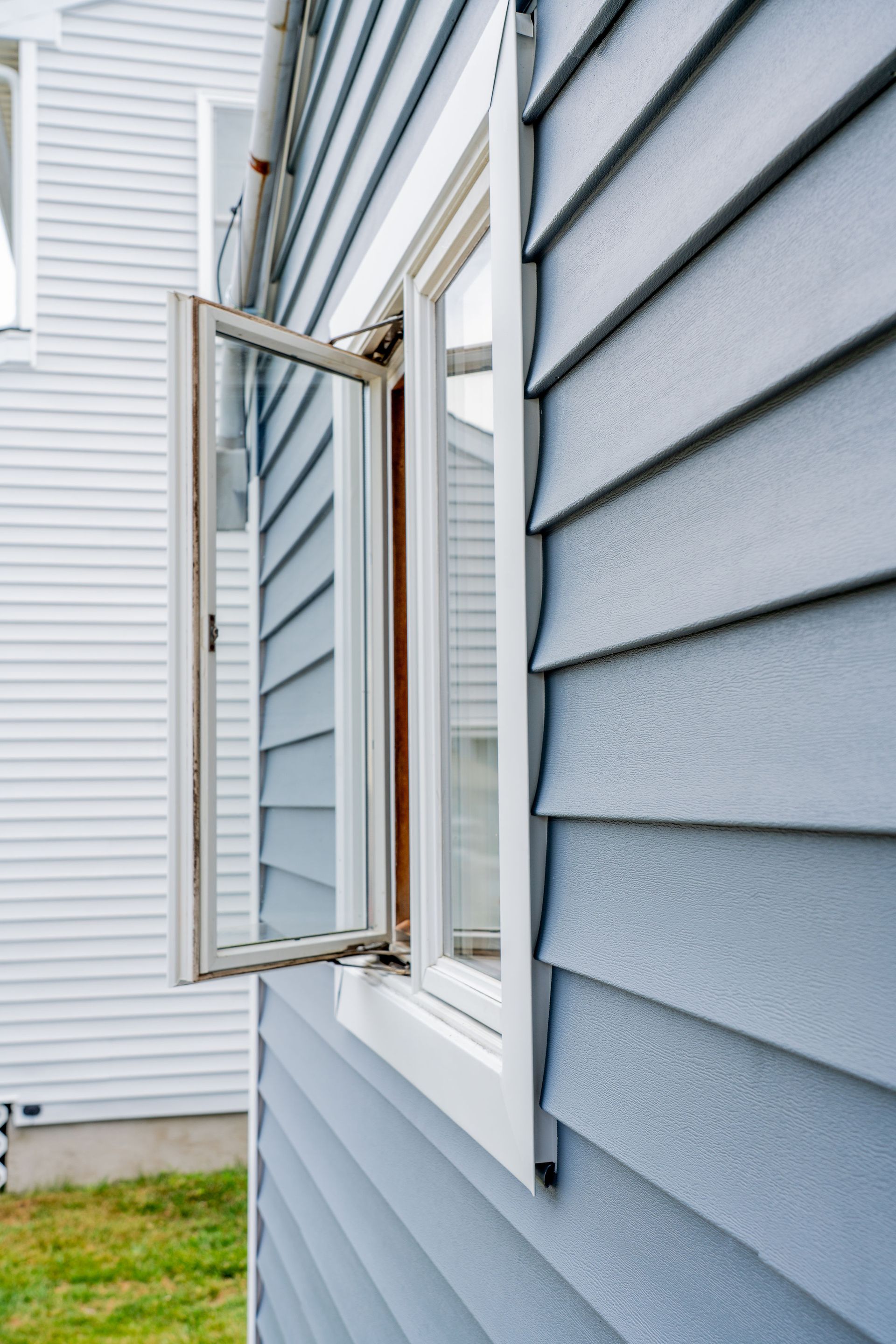 Open window on a blue house exterior with white trim and vinyl siding