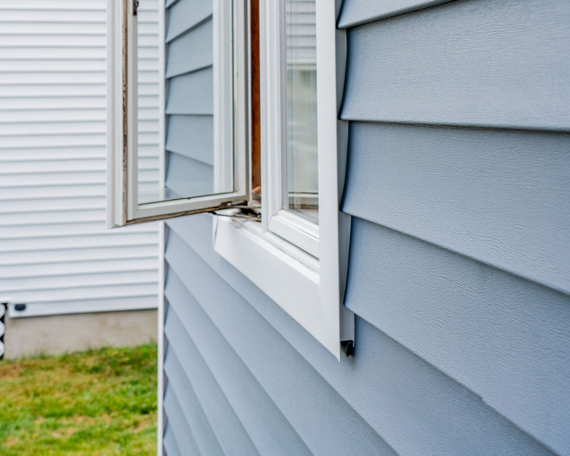 Open window on a gray-sided house exterior beside a white neighboring wall.