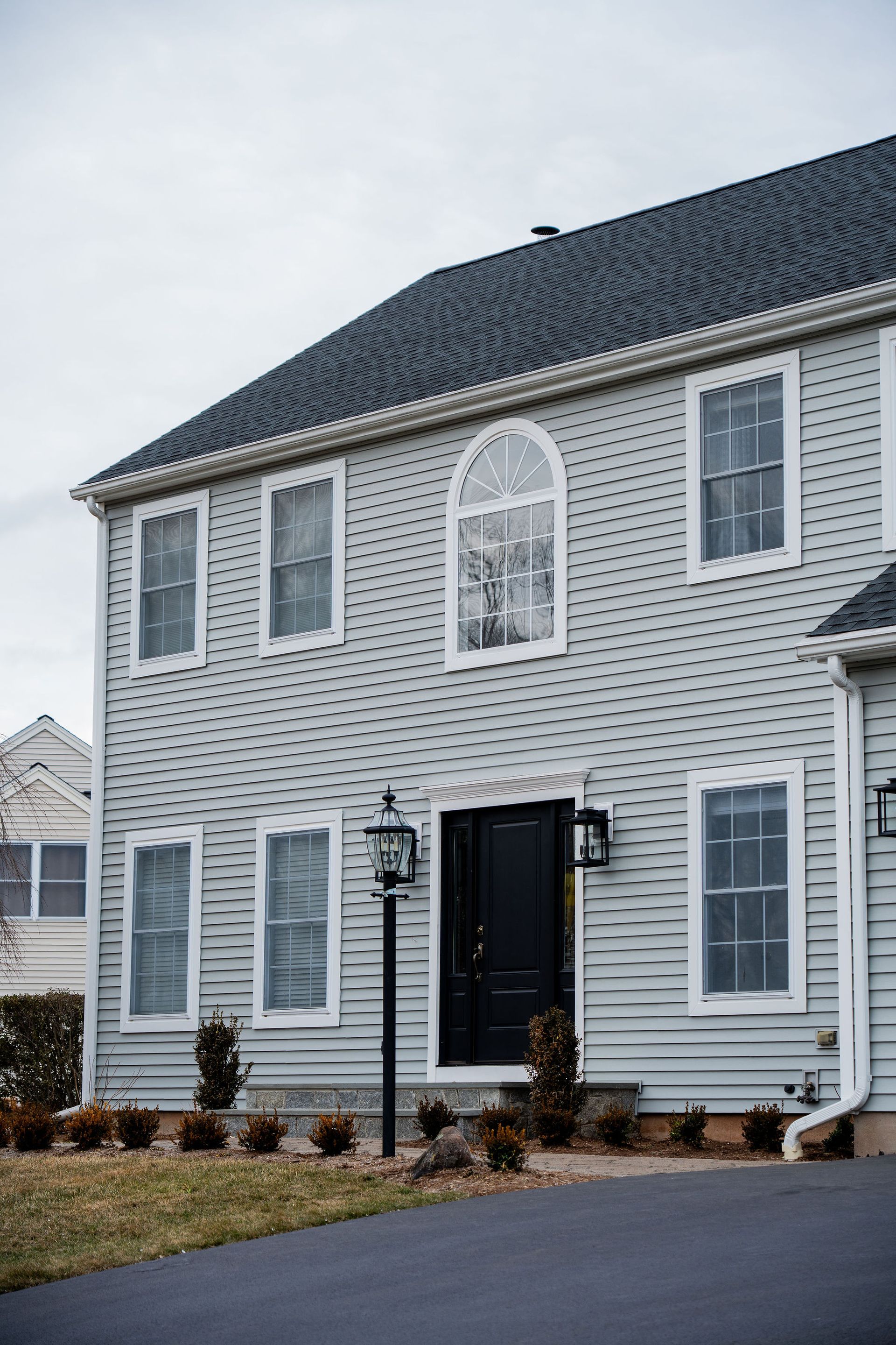 Two-story light blue house with black door, arched window, and several other windows; a black driveway and dark roof.