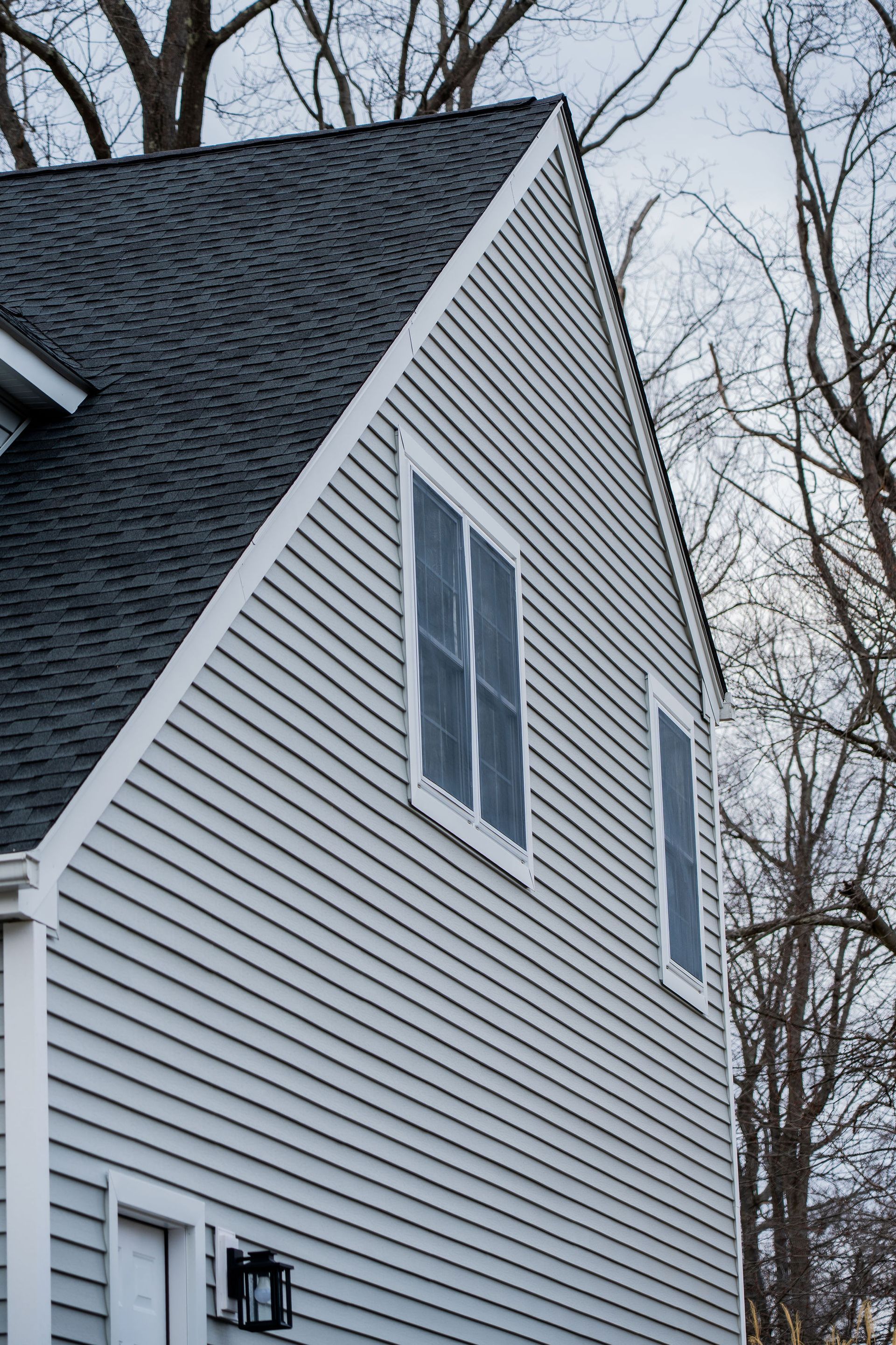 Gray house exterior with dark shingled roof, windows, and light gray siding.