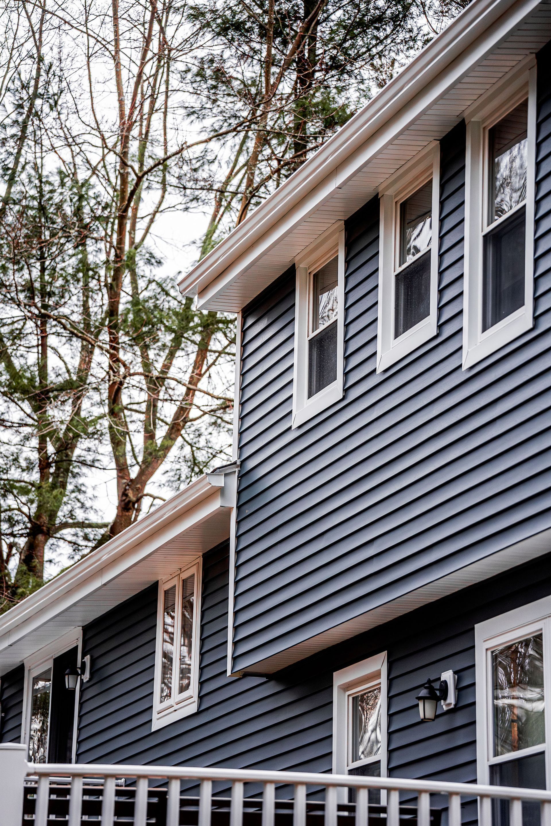 Blue siding on a two-story house with white trim and windows, surrounded by trees.