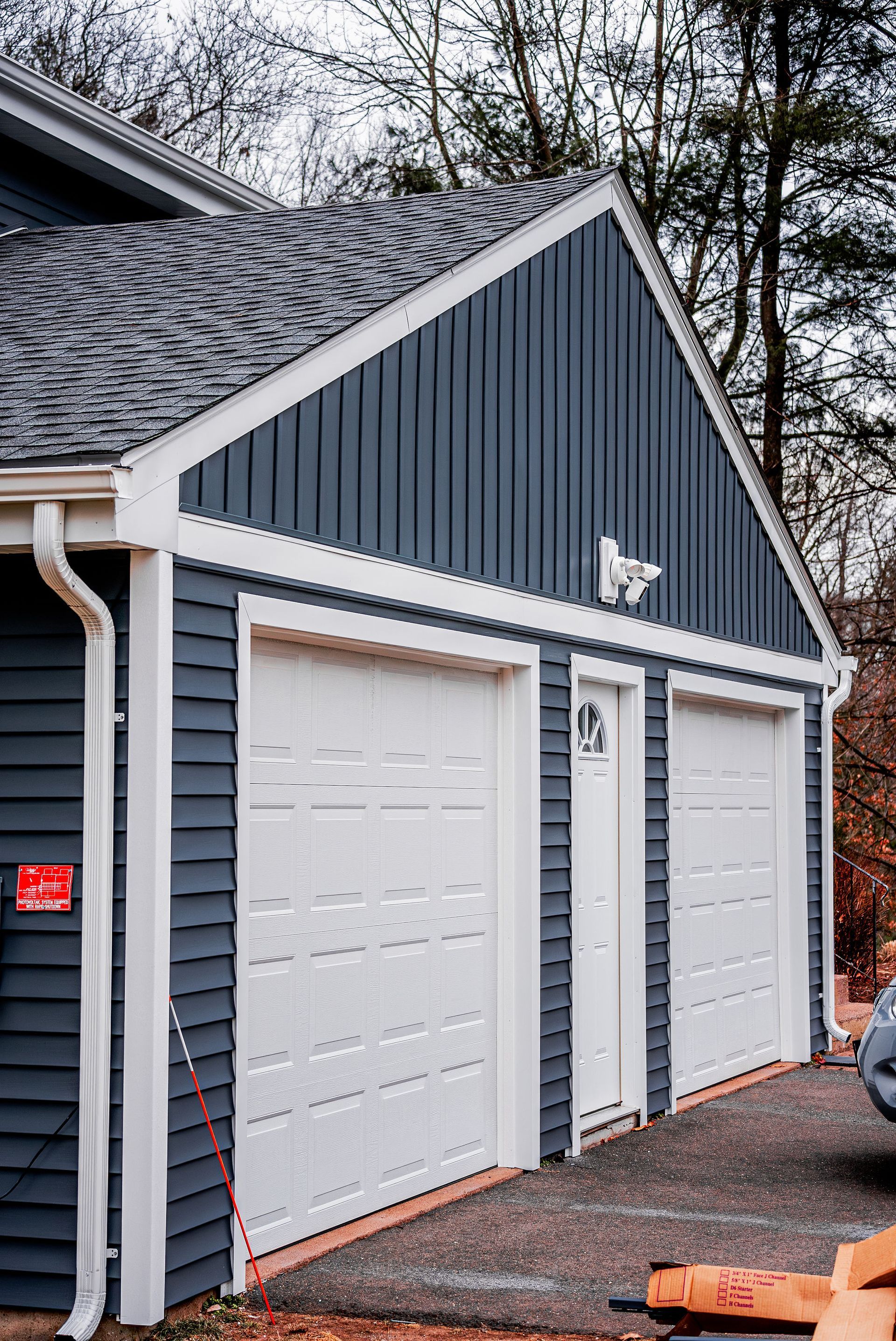 Blue-sided garage with white doors, gutters, and trim under a gray roof.