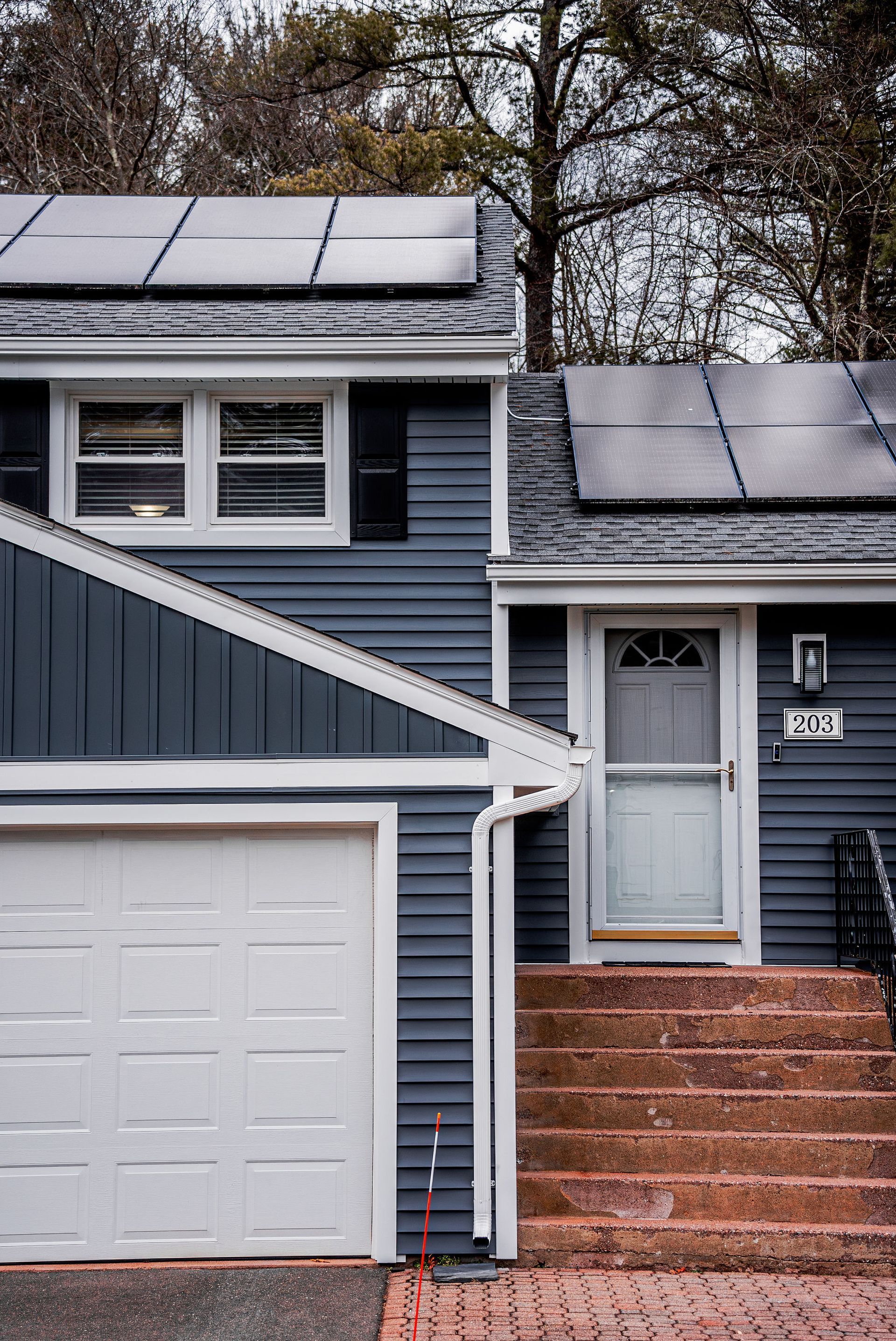 Blue house with solar panels on the roof, white garage door, and brick steps leading to the front door.