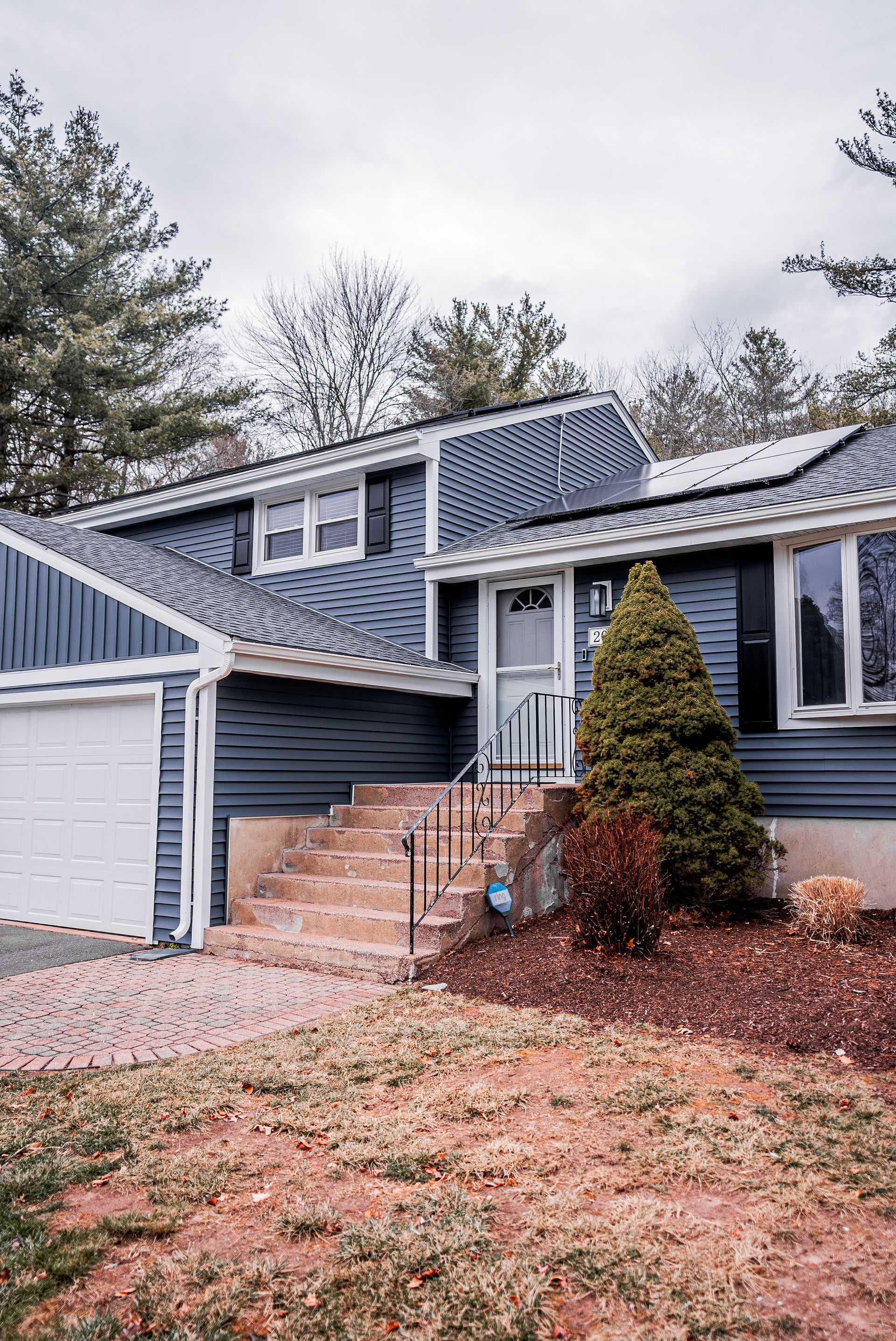 Blue house with a white garage, stairs, and a small front yard with dry grass.