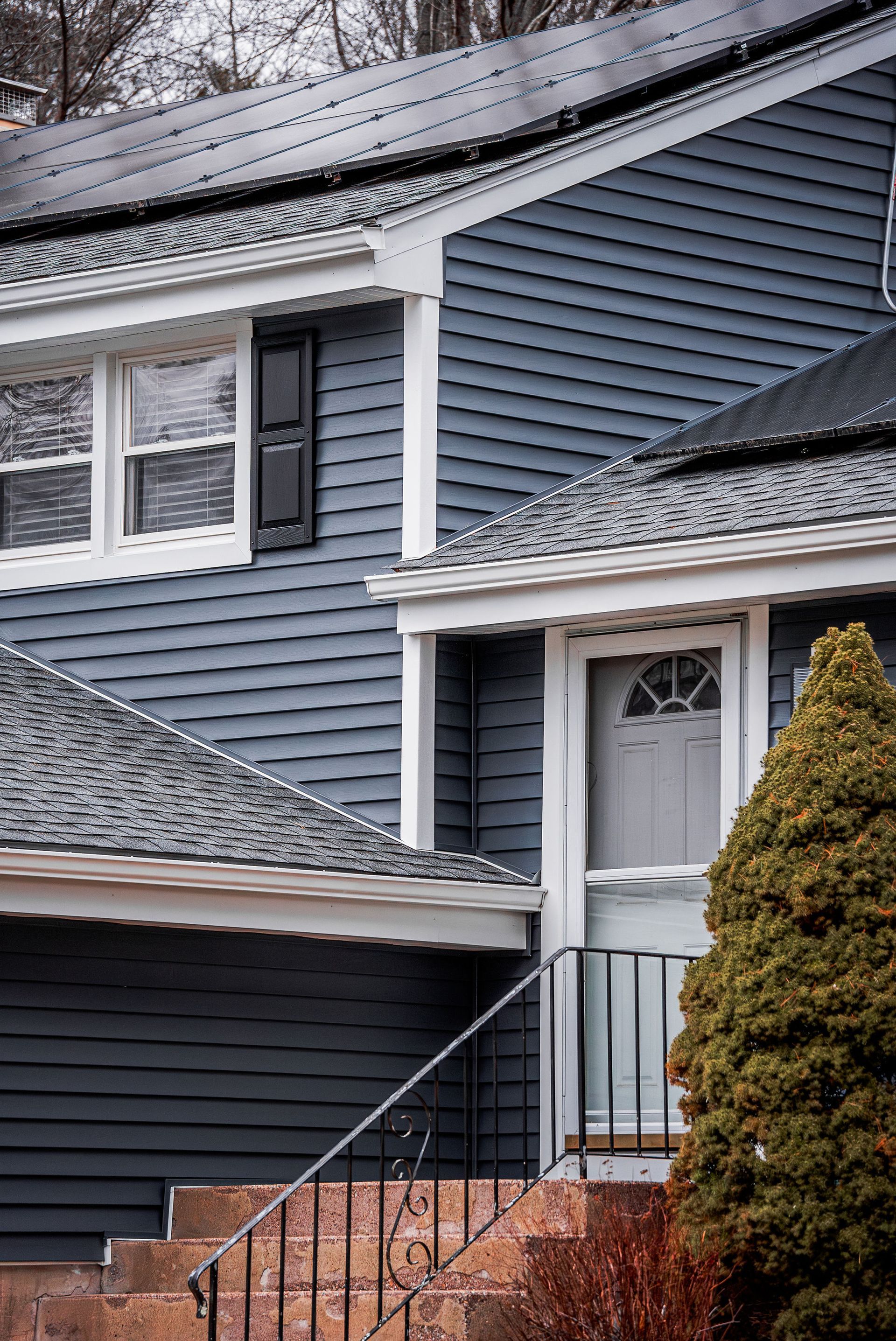 Blue-sided house with white trim, gray roof, black shutter, and front door with small steps.