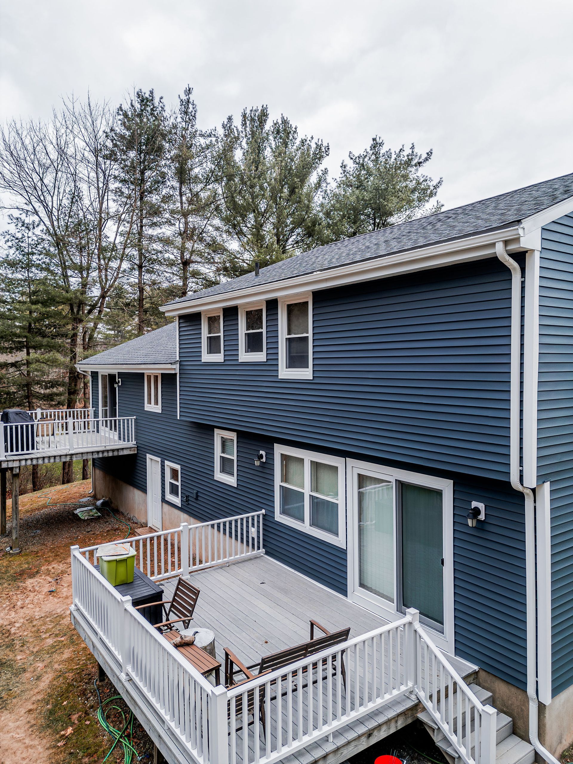 Two-story house with dark blue siding, white trim, and multiple decks surrounded by trees.