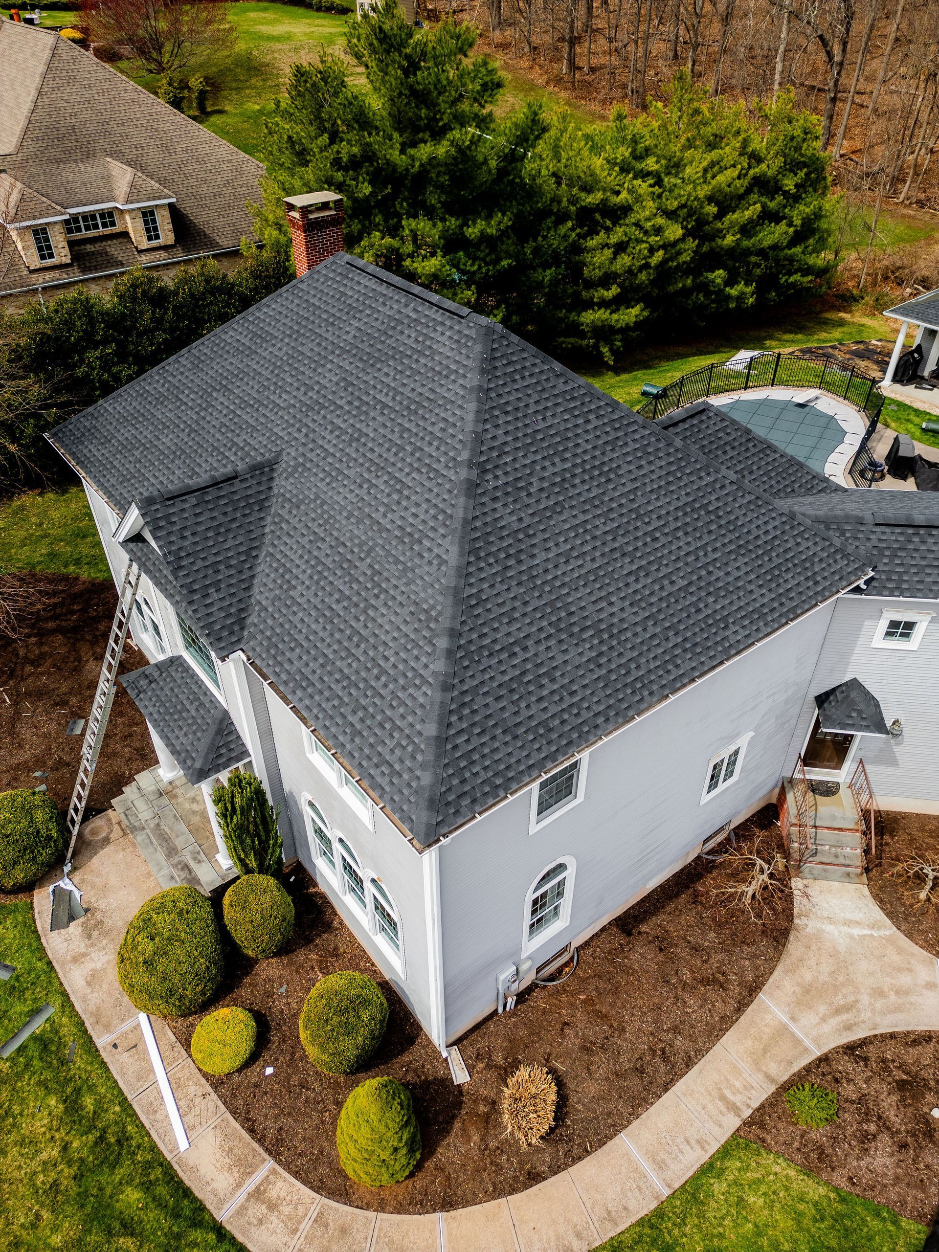 Gray house with dark gray roof, landscaping, and a swimming pool in a yard.