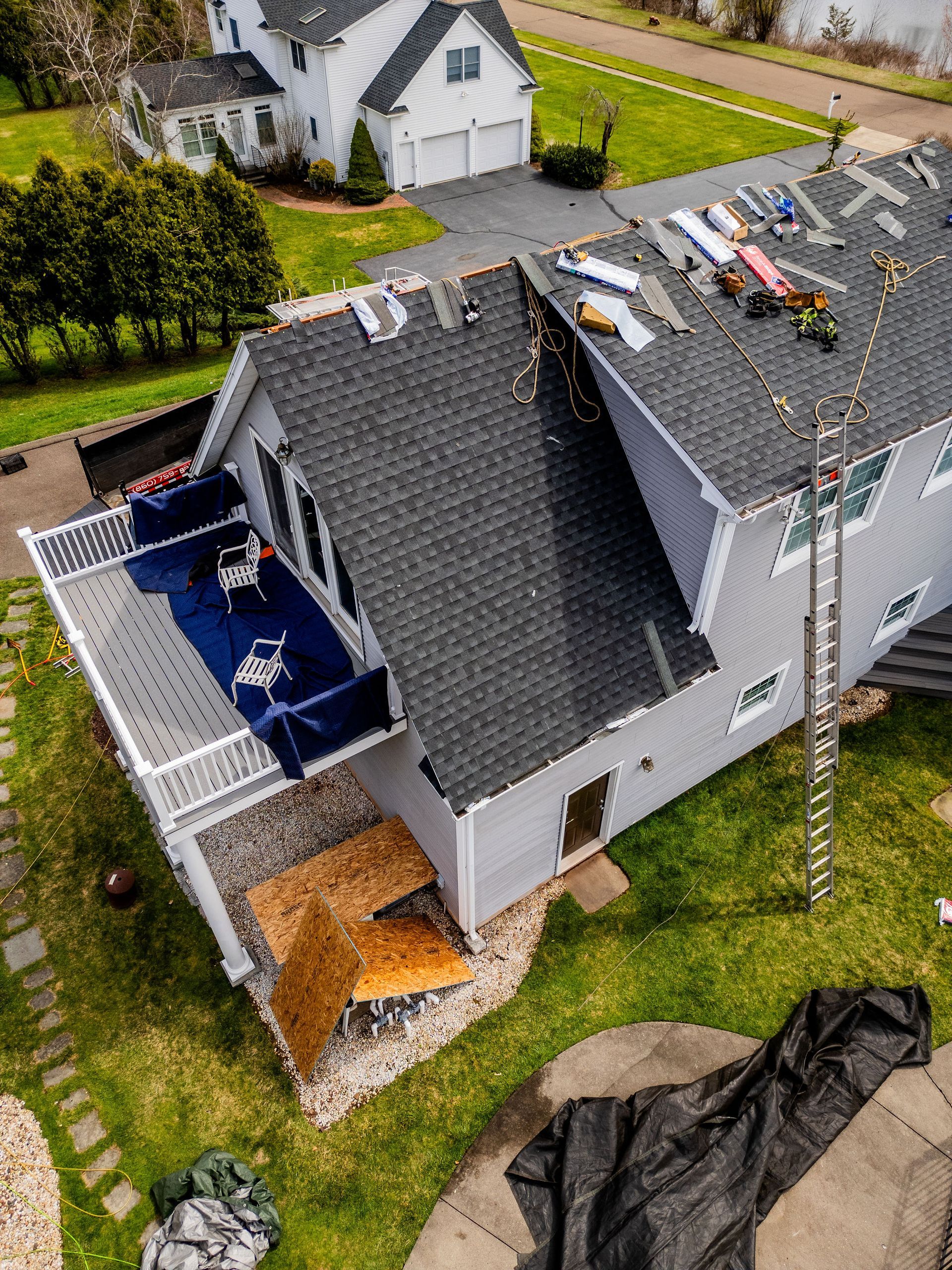 Damaged roof of a gray house with a deck. Debris scattered on the roof. Ladder leans against the side.