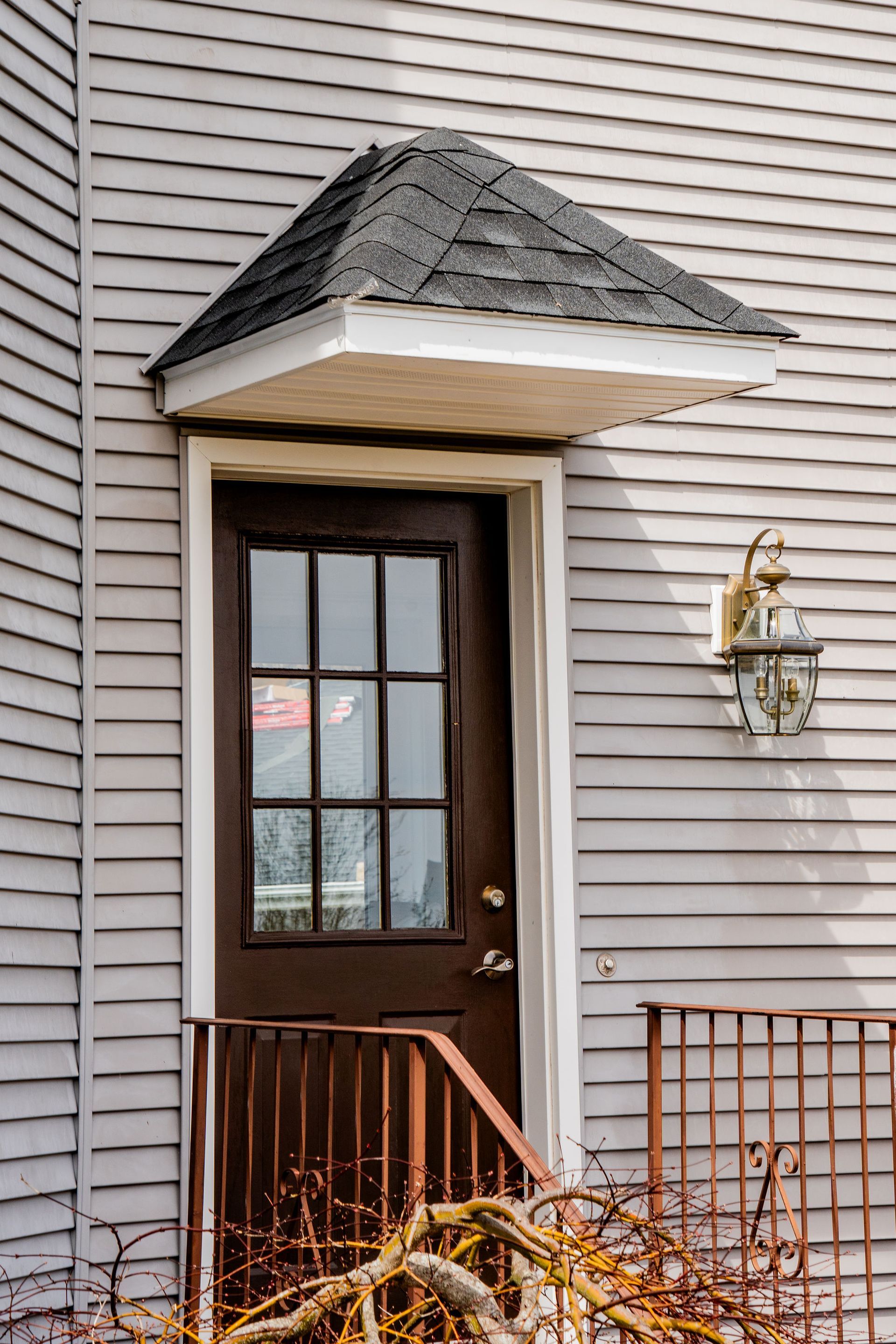 Brown door with small triangular roof, white trim, and a decorative light on a gray clapboard building.