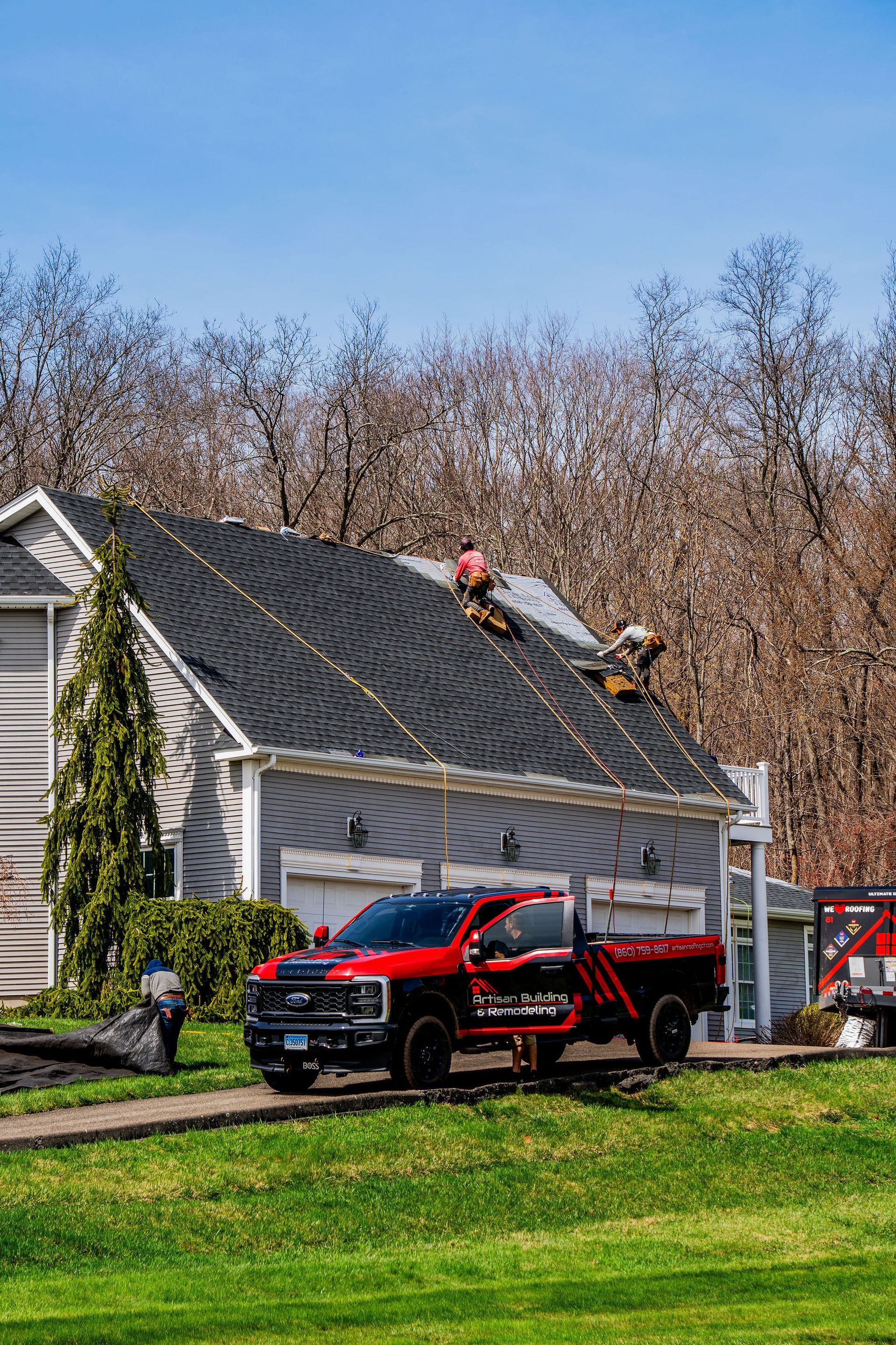 Red truck parked by house, roofers on roof, trees in the background.