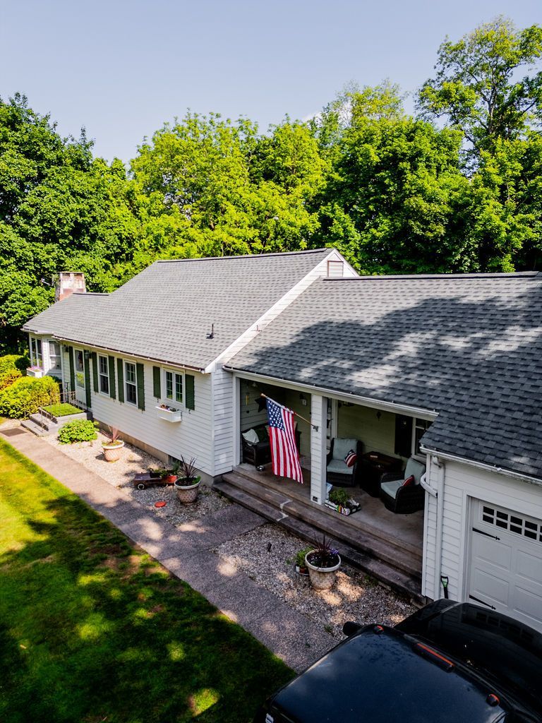 White house with an American flag hanging on the porch, nestled in a green treeline.