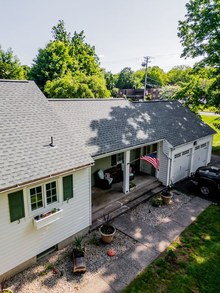 White house with gray roof, green shutters, porch with American flag, and three-car garage.