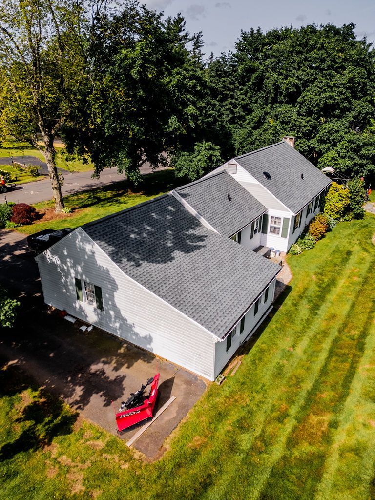 Aerial view of a white house with a gray roof and green lawn, parked red vehicle.