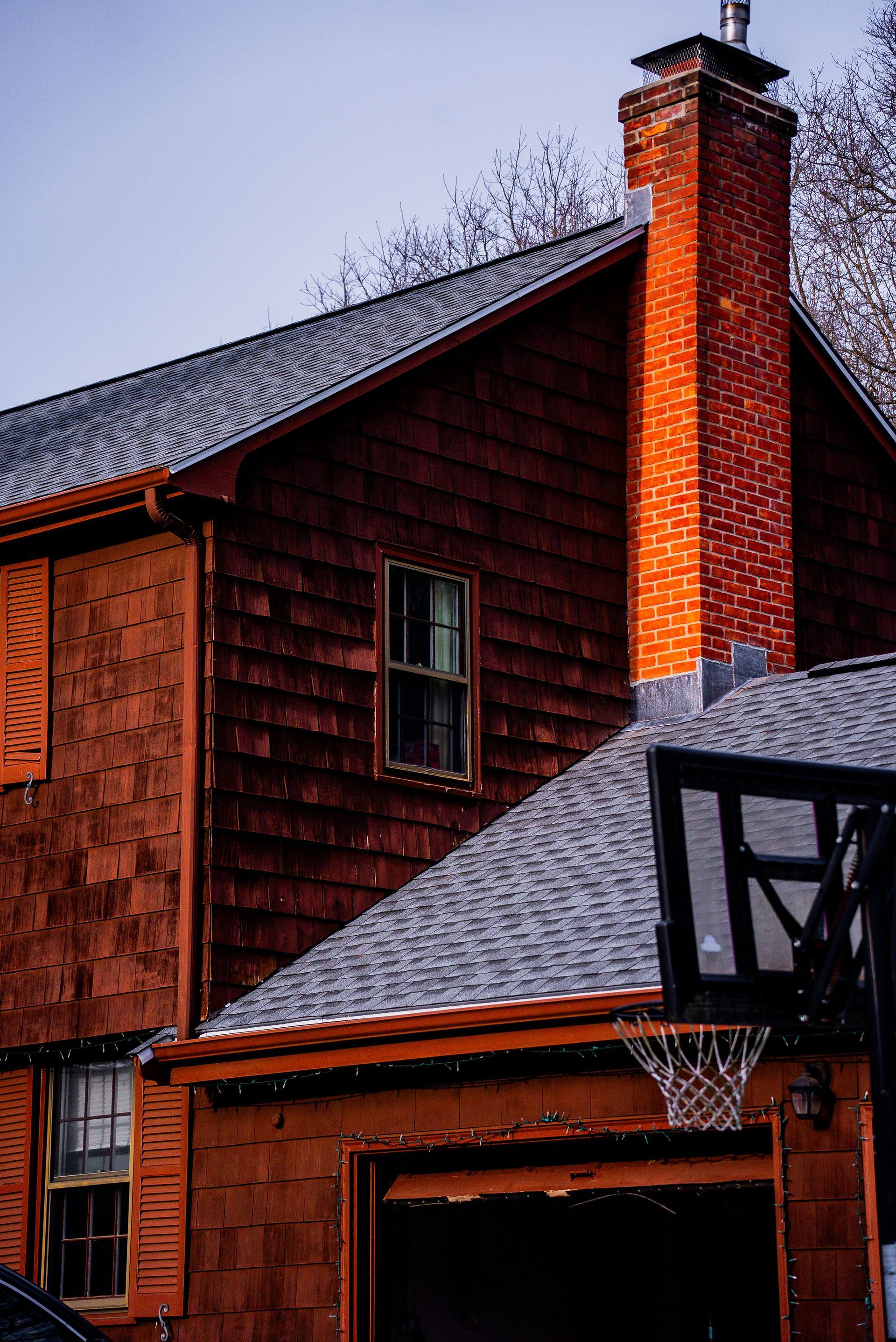 Brown house with a brick chimney; a basketball hoop is in the foreground.