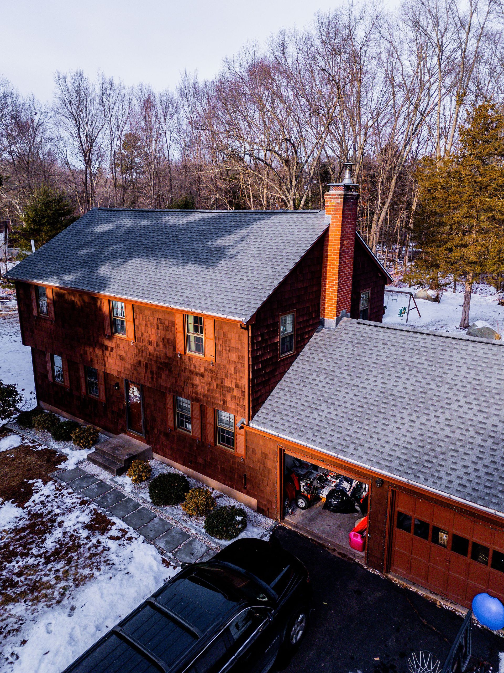 Two-story wood-sided house with attached garage, snow on ground, car parked in front.