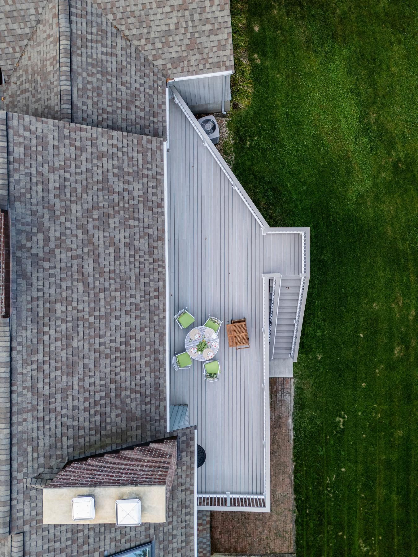 Overhead view of a house with a gray deck, outdoor furniture, and green lawn.