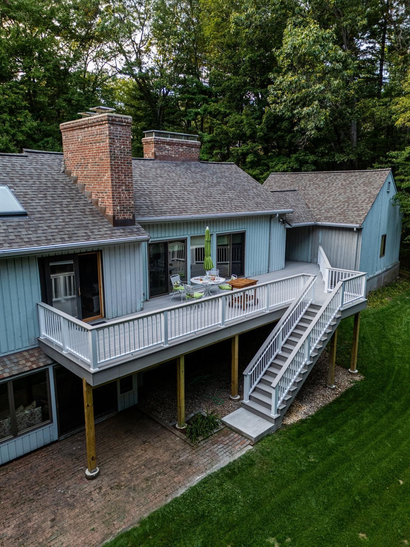 Blue house with brick chimney, deck, stairs, and backyard with green grass.