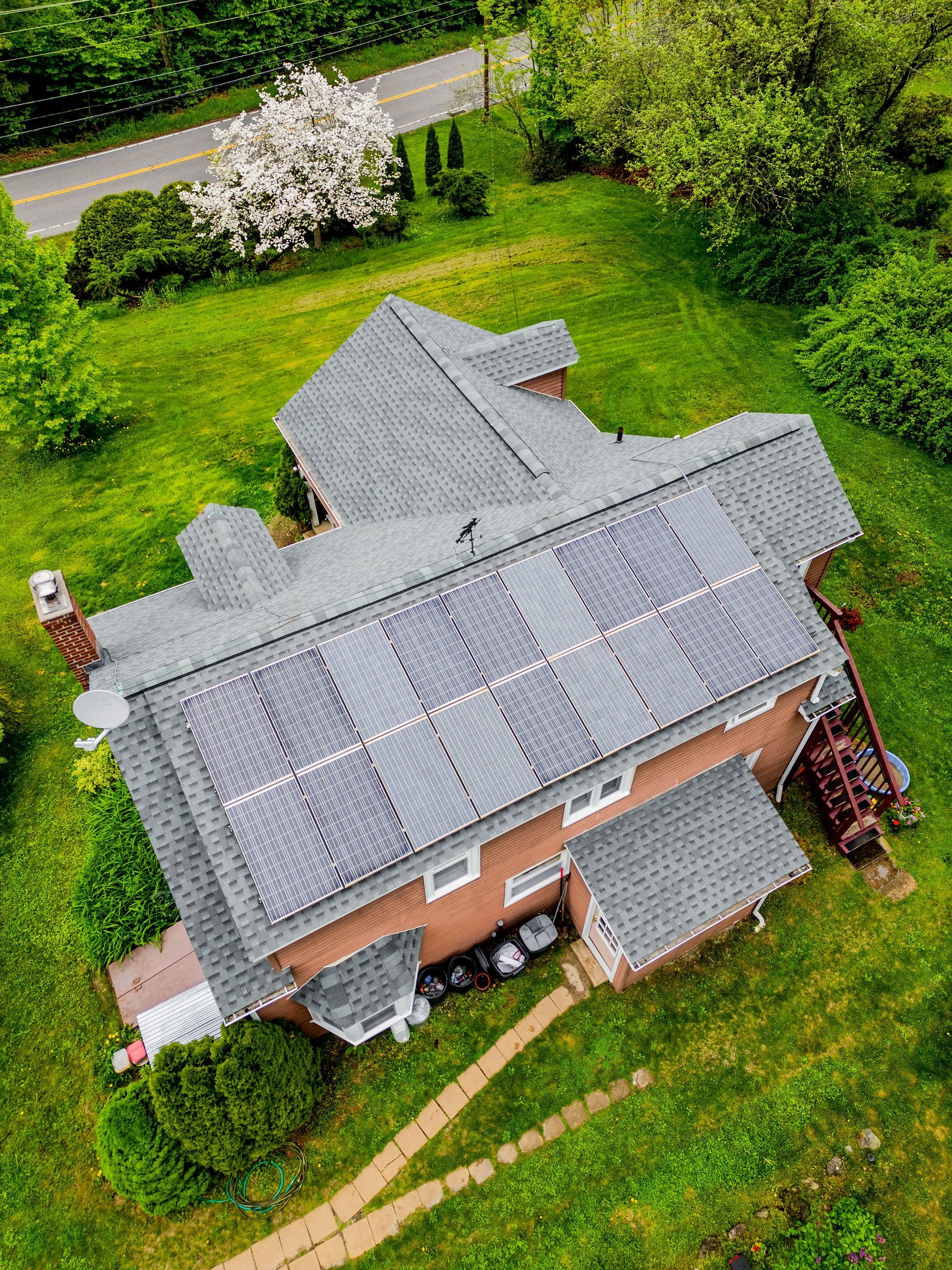 Aerial view of a house with solar panels on the roof and lush green lawn.