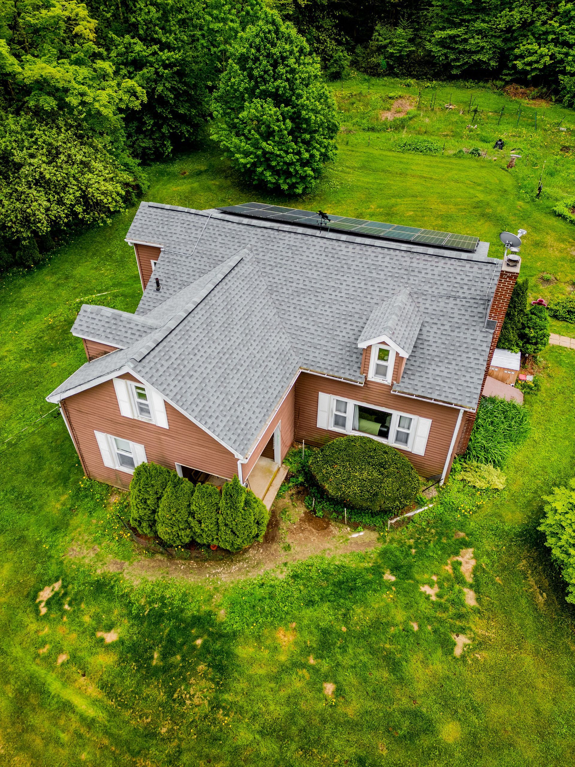 Brown house with gray roof surrounded by green grass and trees.