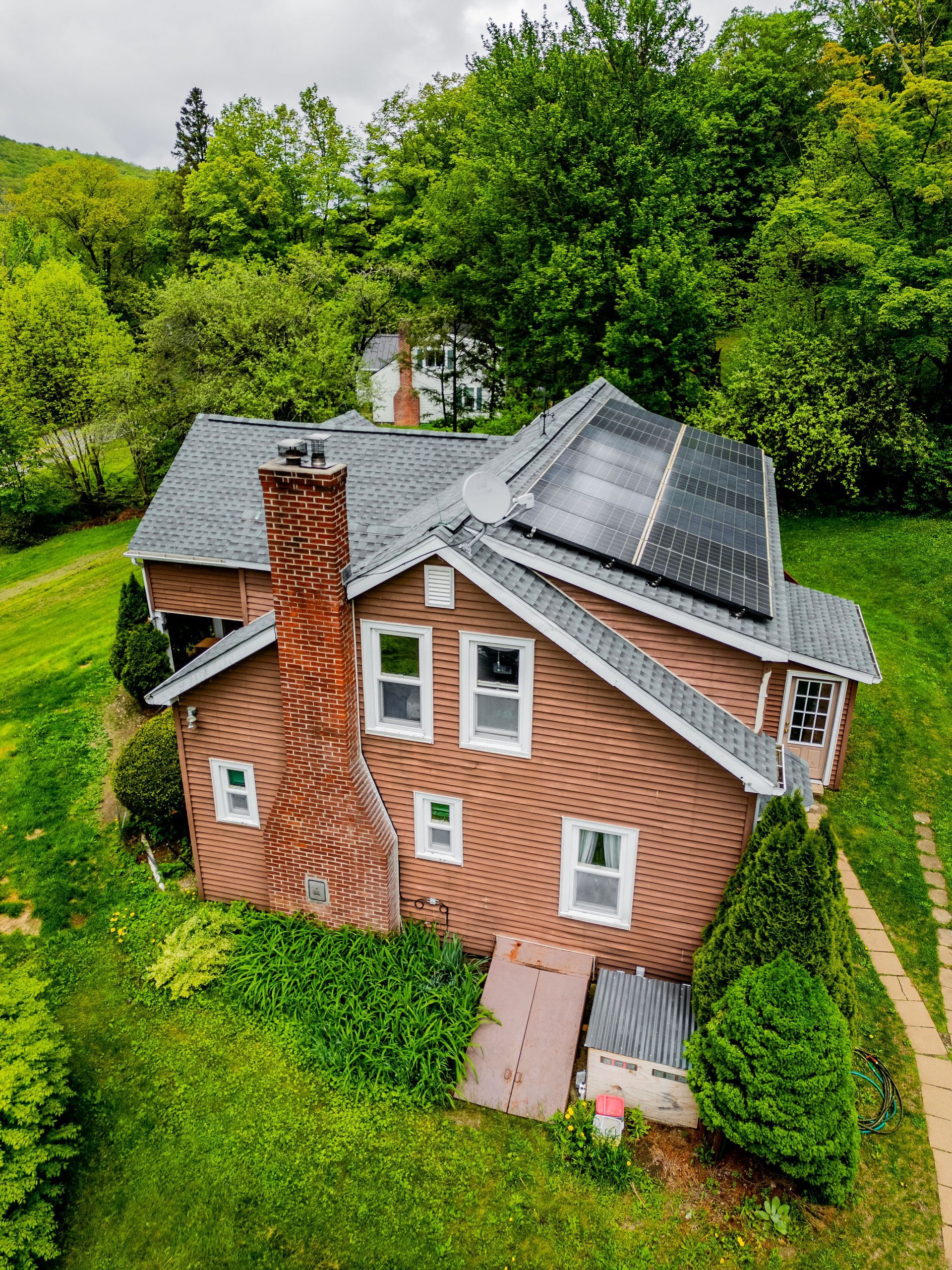 Red brick house with solar panels on roof, large brick chimney, surrounded by green grass and trees.