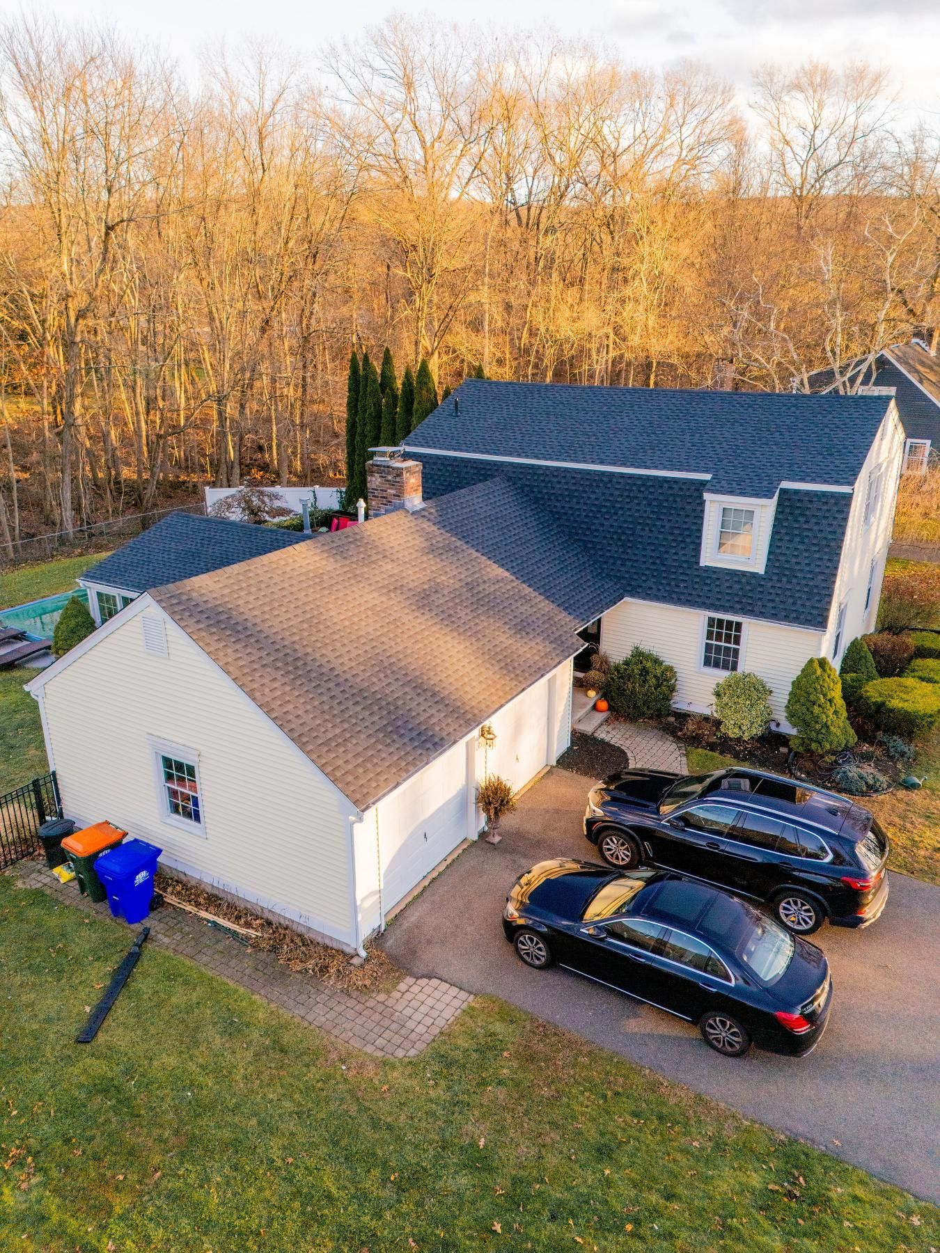 House with two-car garage, two black cars parked in driveway, green lawn, trees in background.