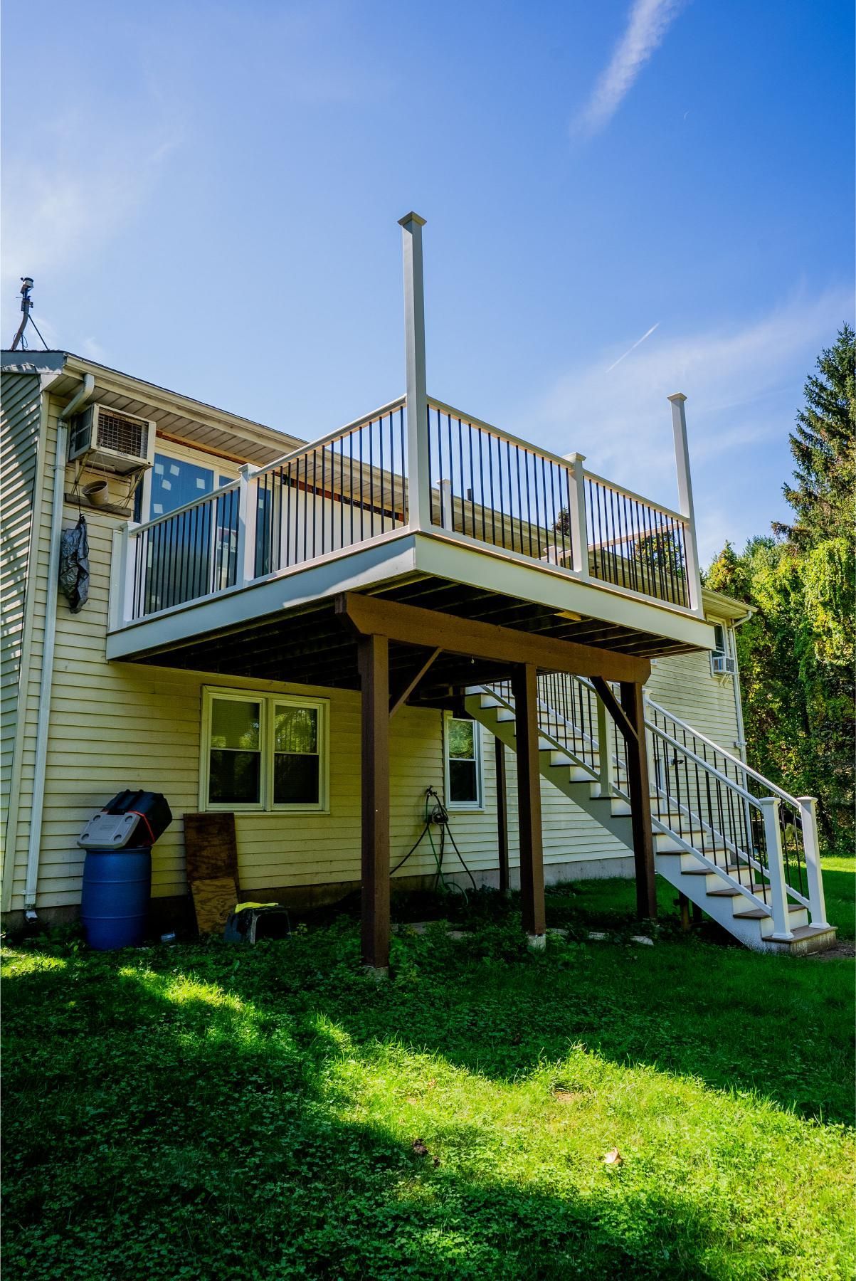 Two-story house with a wooden deck and stairs. Green grass and blue sky.