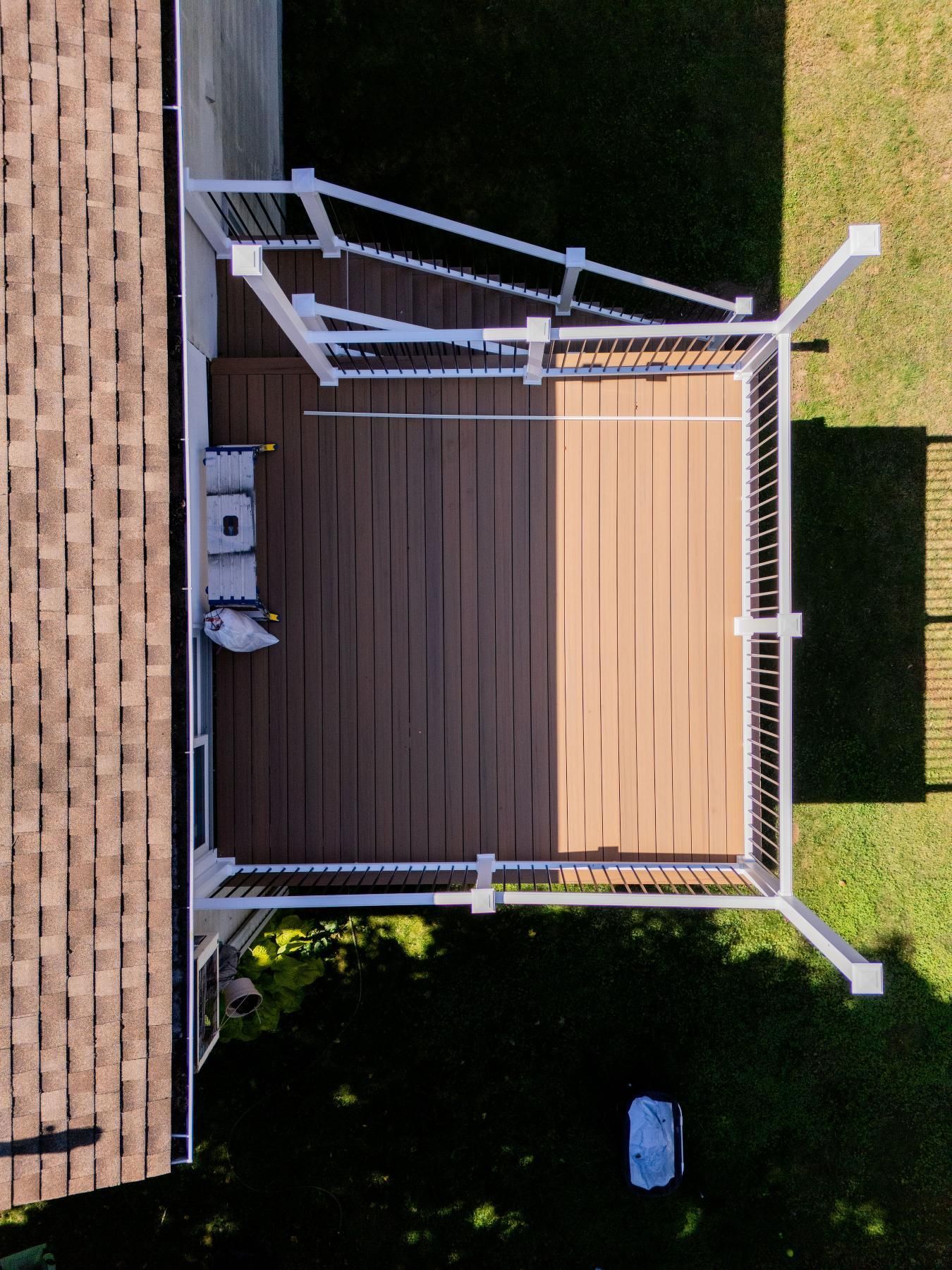 Overhead view of a composite deck with white railings, half in sunlight, with a grill and side table.