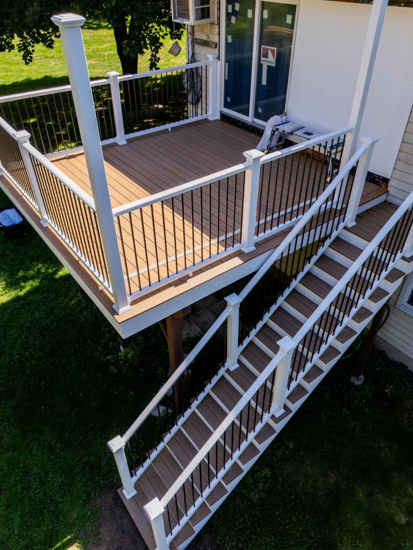 A newly built deck with stairs attached to a house. White railings with black bars, brown deck.