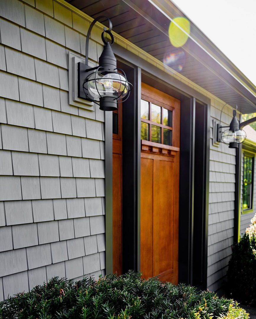 Gray shake-sided house with a wooden door framed in black. Lanterns flank the door.