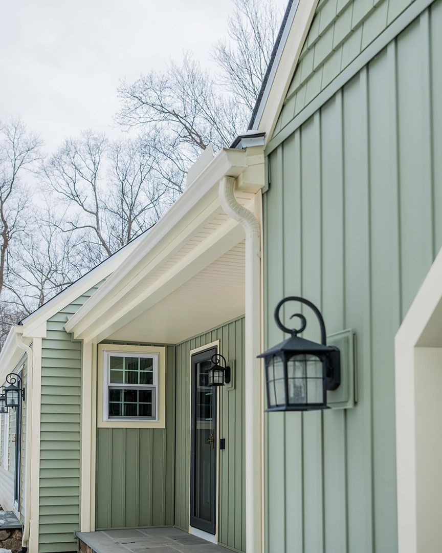 Green house exterior with black front door, window, and wall sconce. White trim and gutter.