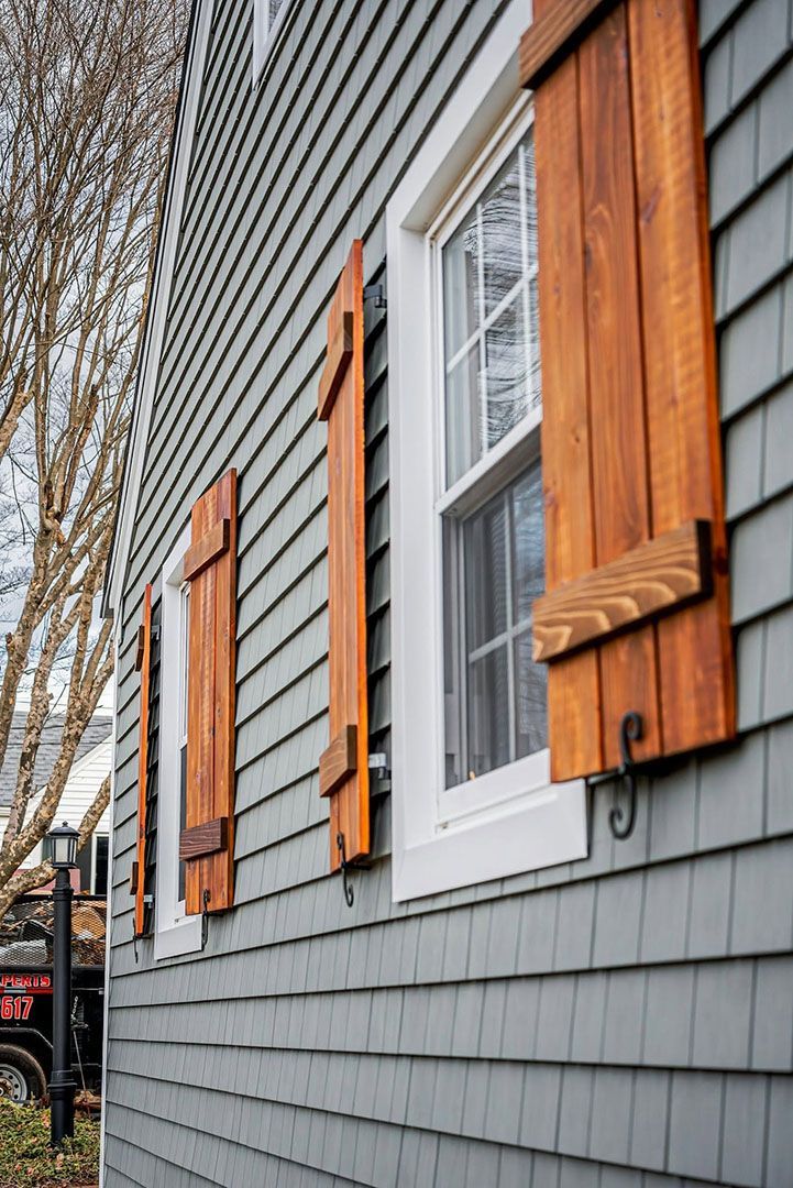 Gray-sided house with three white-framed windows and wooden shutters.