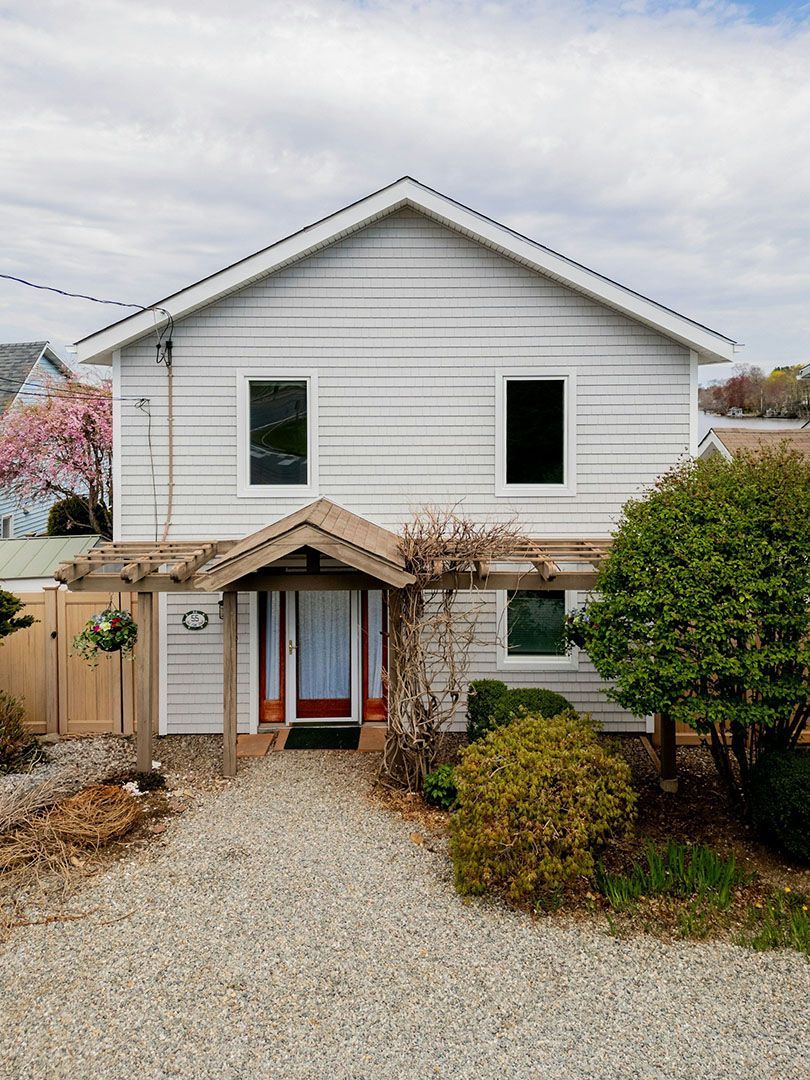White two-story house with a small porch, windows, and gravel pathway leading to the front door.
