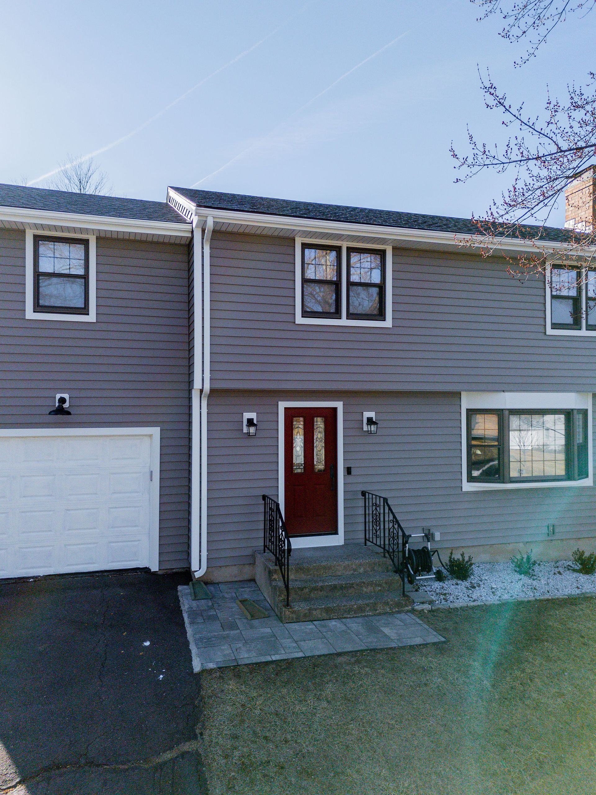 Gray house with red door and white garage door. Black trim on windows. Stone walkway leads to the entrance.