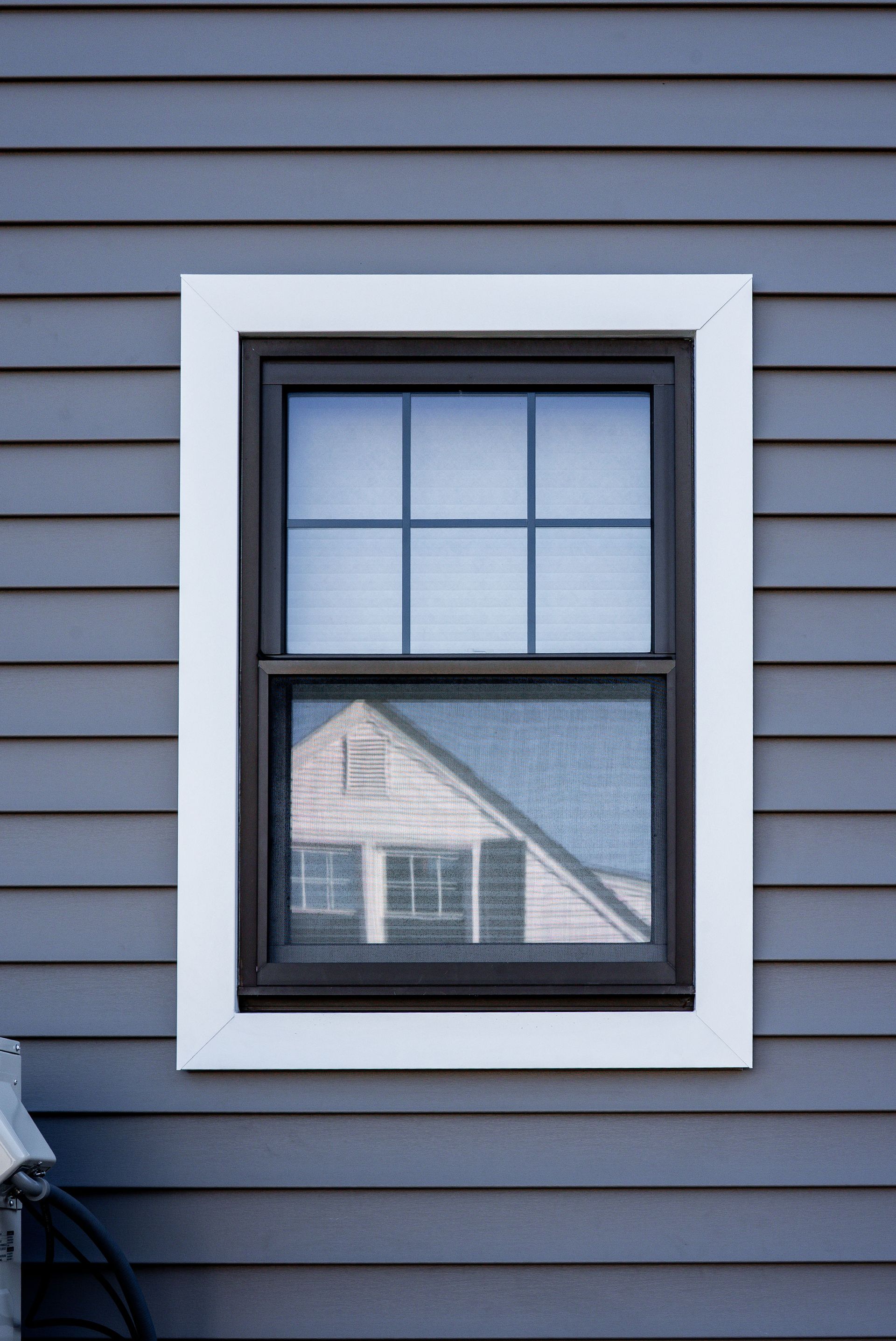 White-framed window on blue siding, with a reflection of a house in the lower pane.