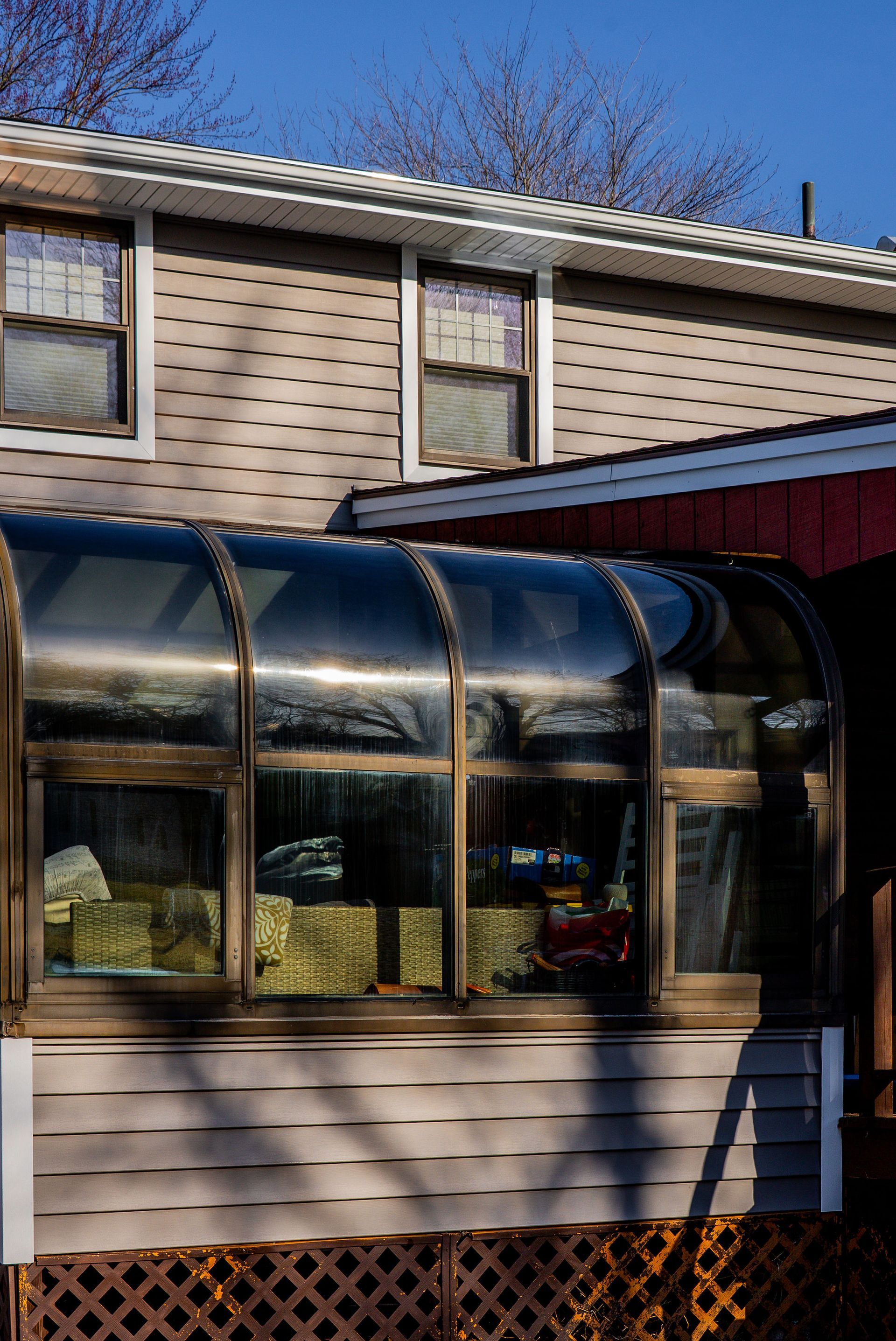 A sunroom with a curved glass roof attached to a two-story building.