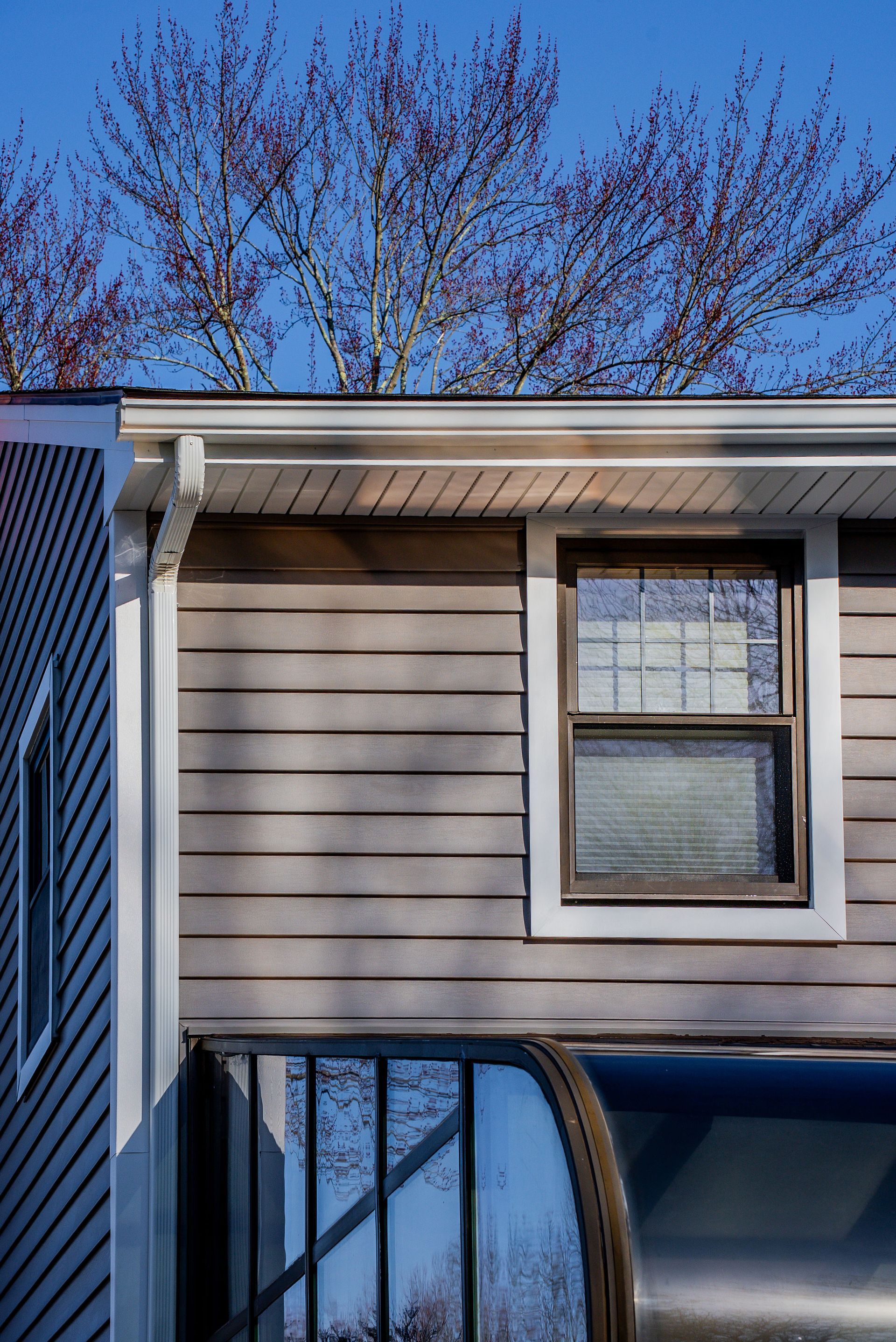 House exterior with tan siding, a window, and a metal awning under a blue sky.