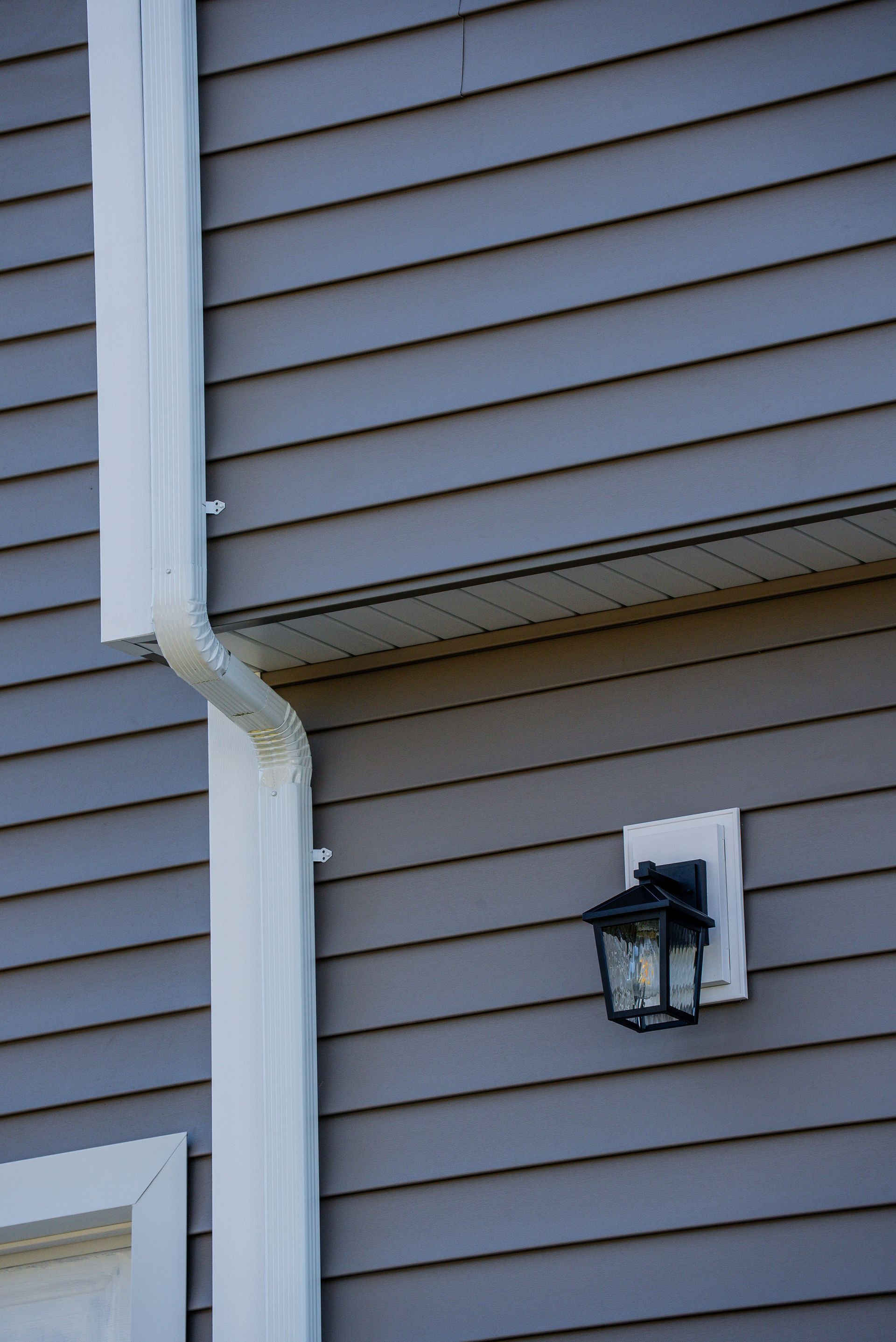 White gutter and lamp on a gray siding house wall.