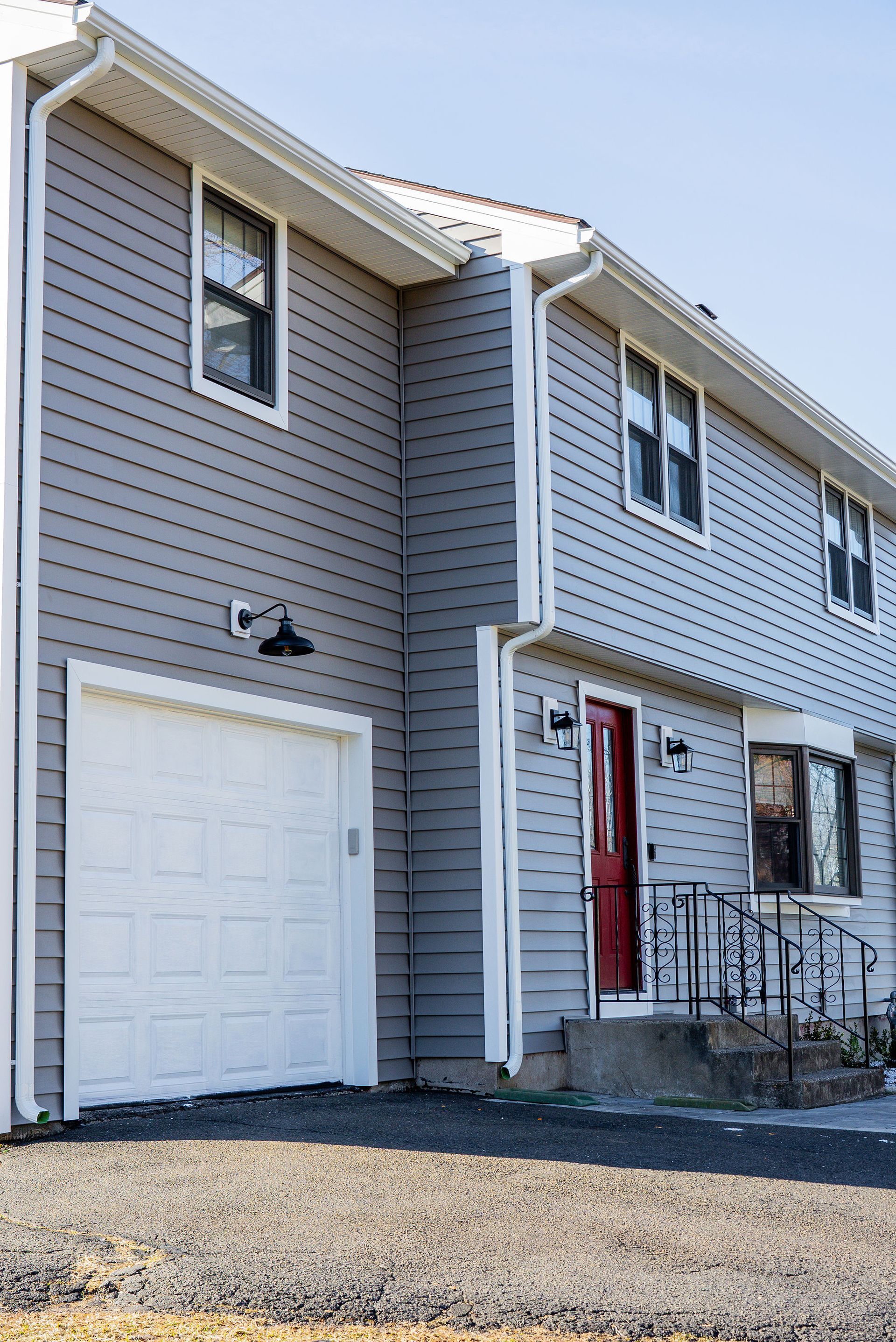 Grey siding two-story townhouse with white trim, garage, and red front door.