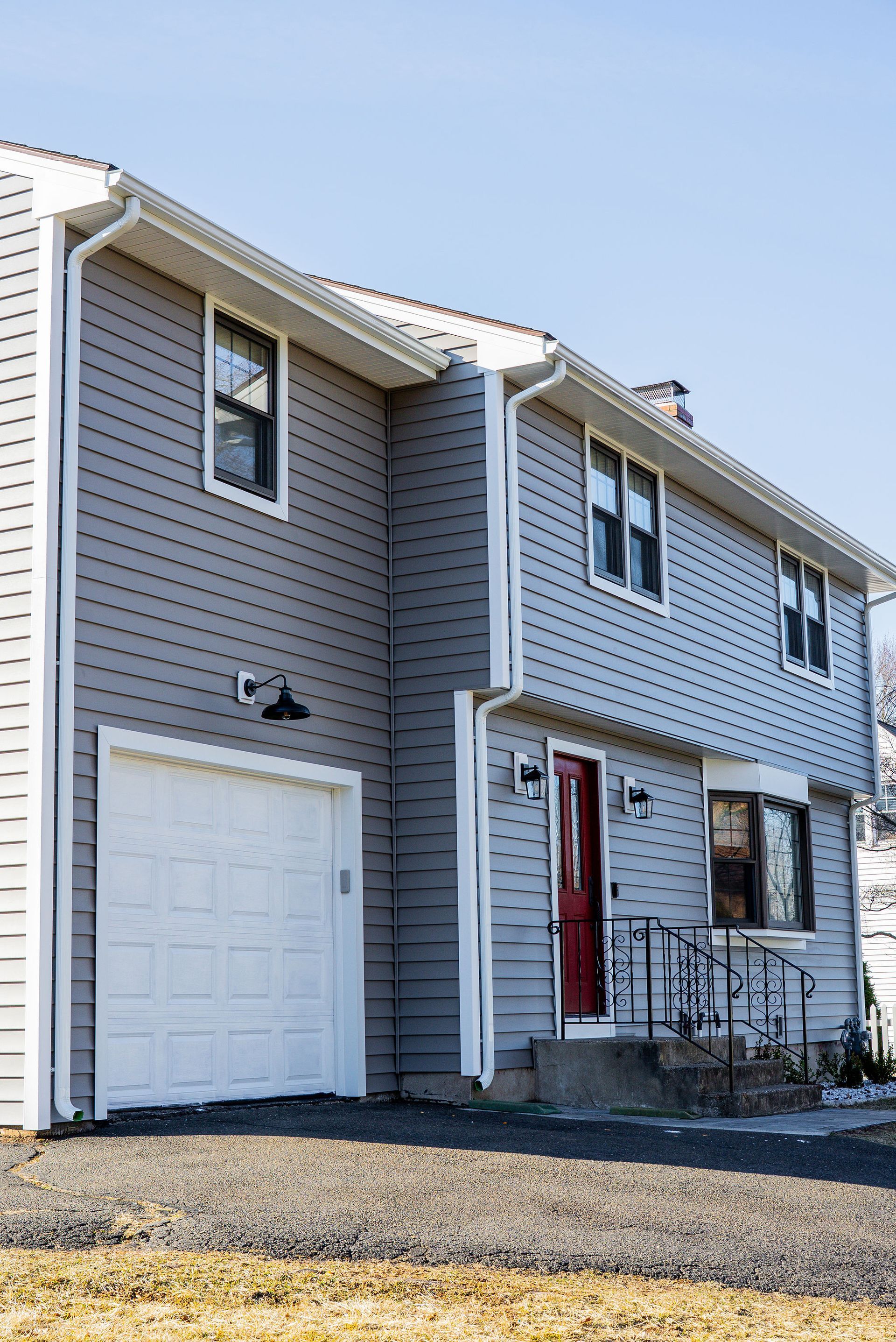 Two-story gray house with white garage door and red front door under a clear blue sky.