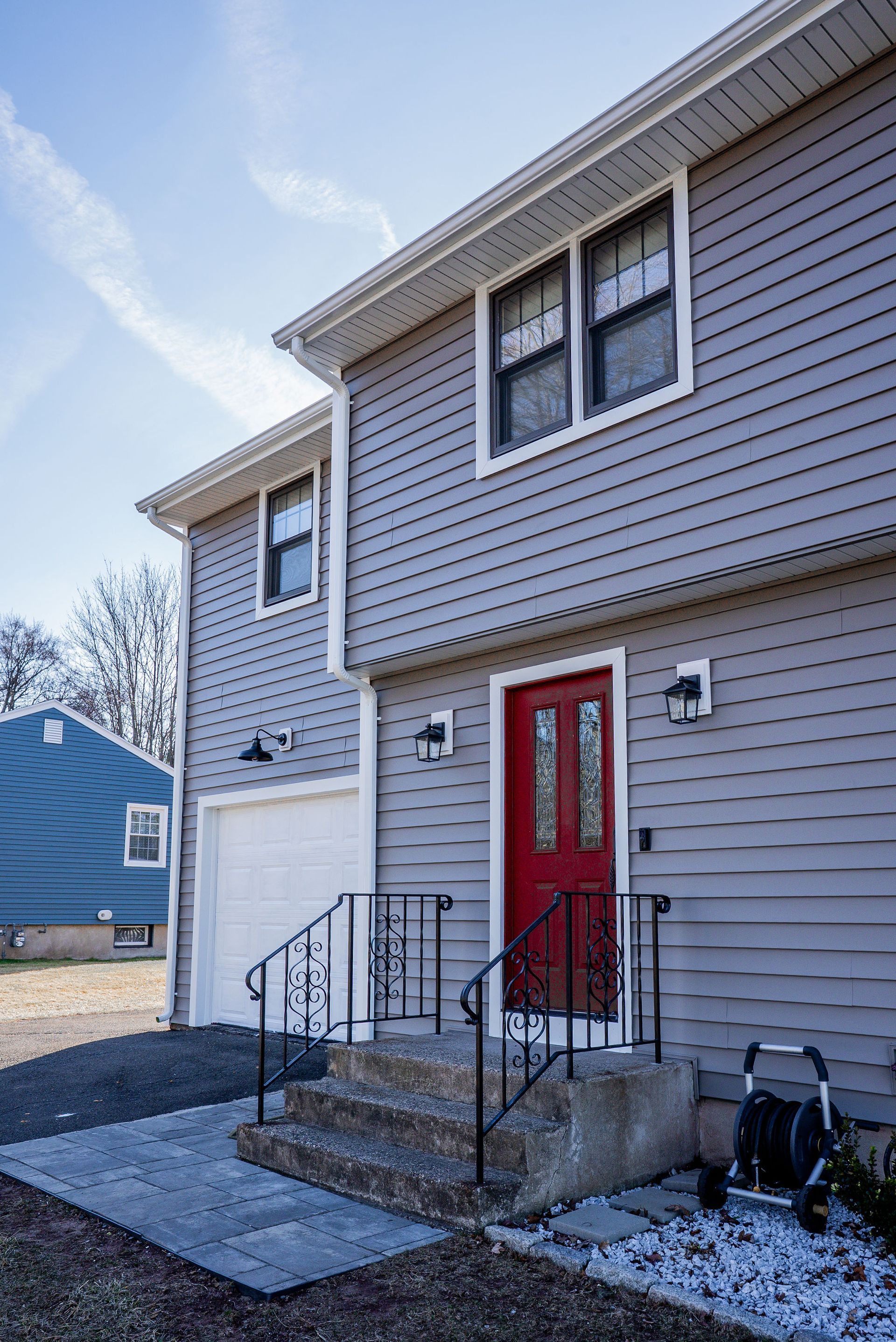 Gray two-story house with a red front door, white garage door, and small front steps with a dark railing.