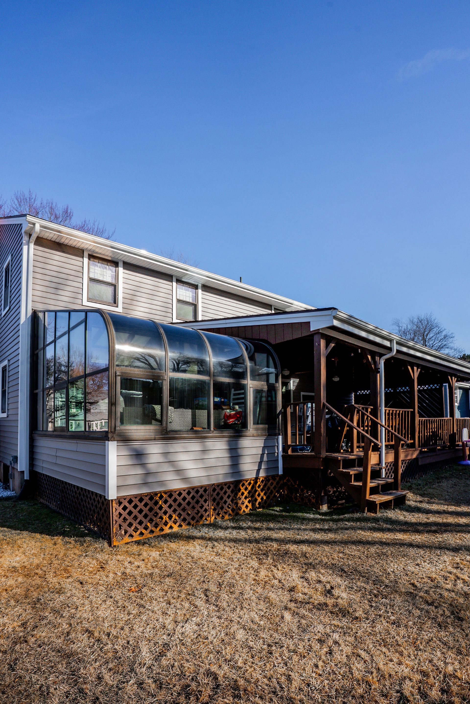 House exterior with a glass-enclosed sunroom and wooden deck under a clear blue sky.