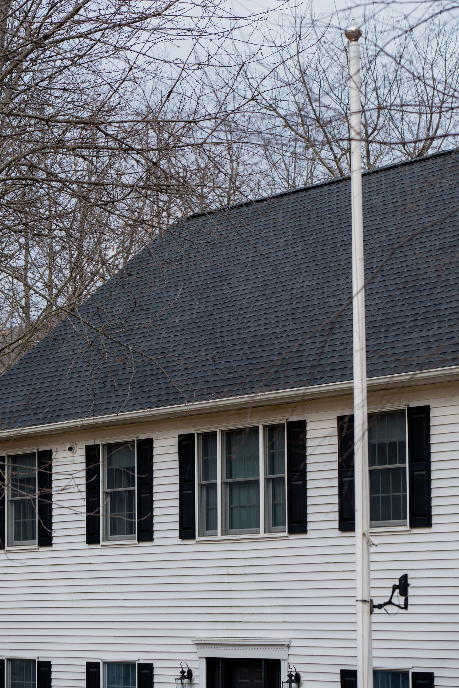 Two-story white house with black shutters and roof. A tall white flagpole is in front of the house.
