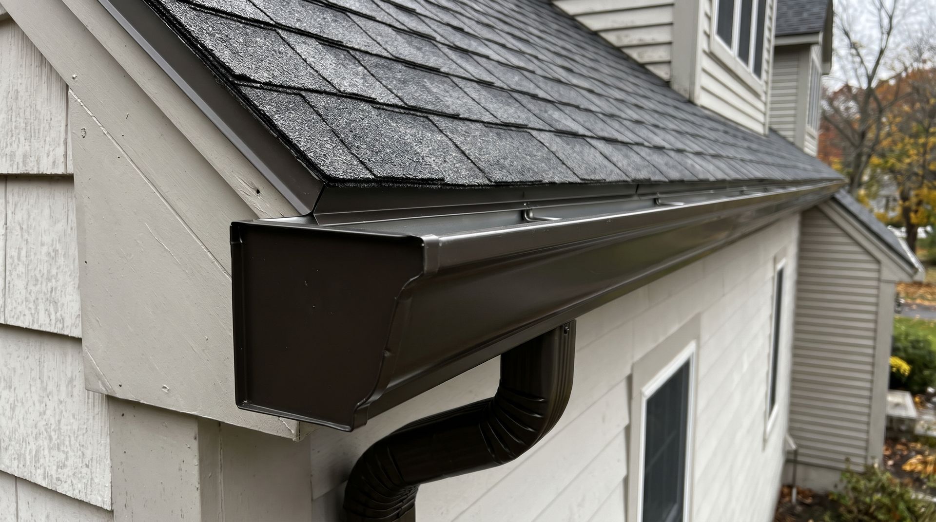 White house gutter and downspout under a beige vinyl-sided roofline