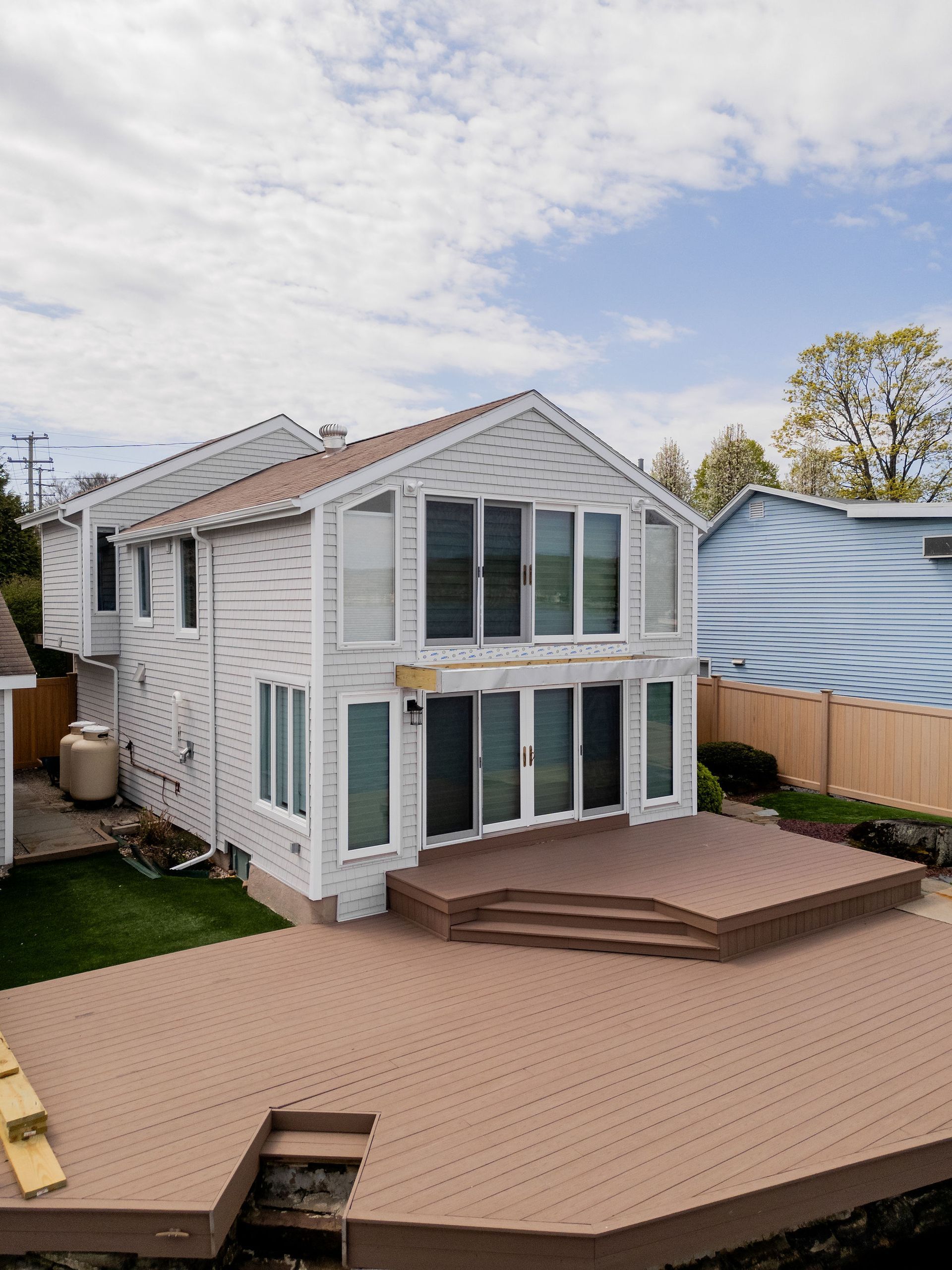 Two-story house with brown deck, multiple windows, and partial blue building visible.