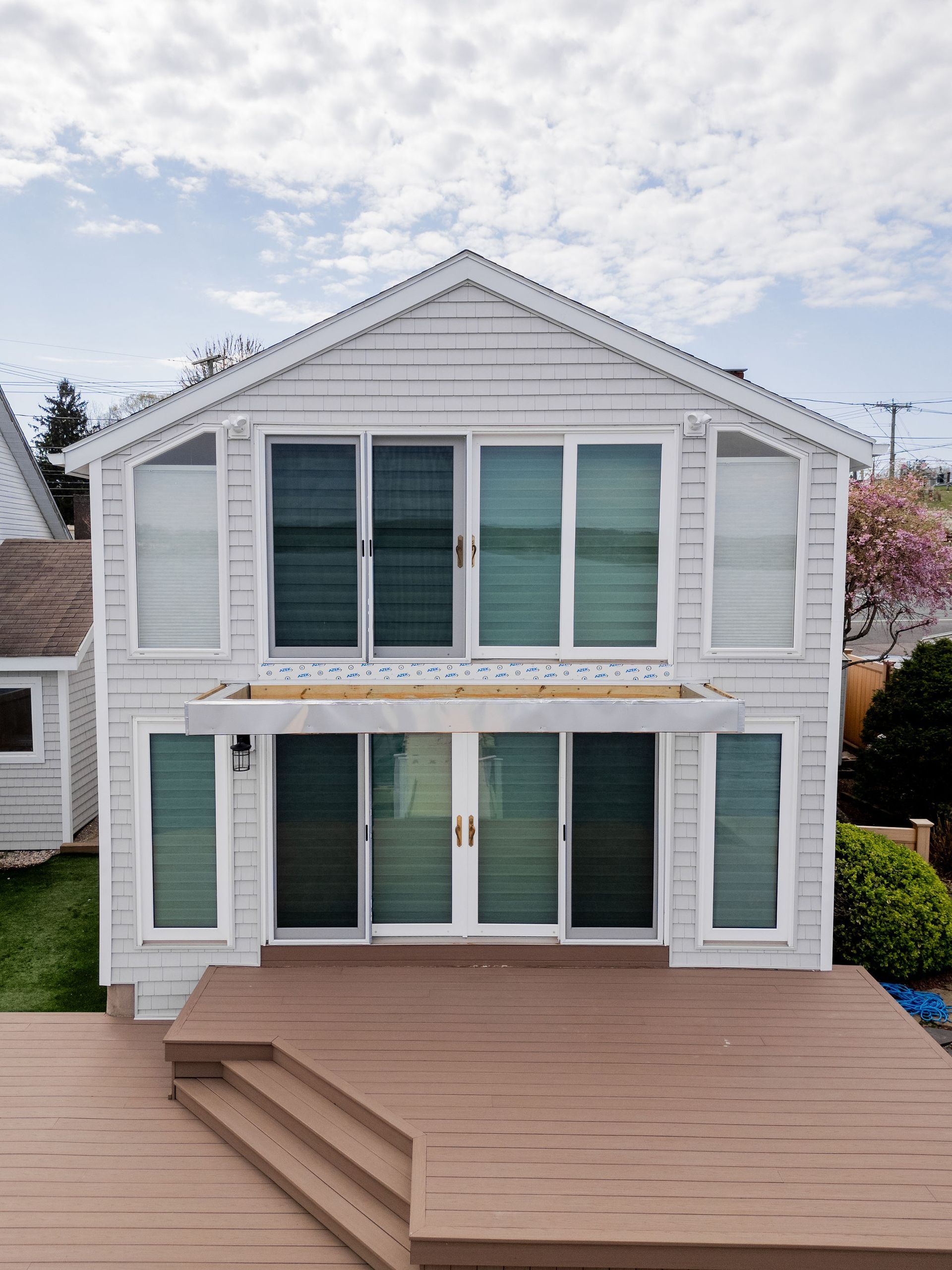 Two-story white house with a brown deck and large windows under a cloudy sky.