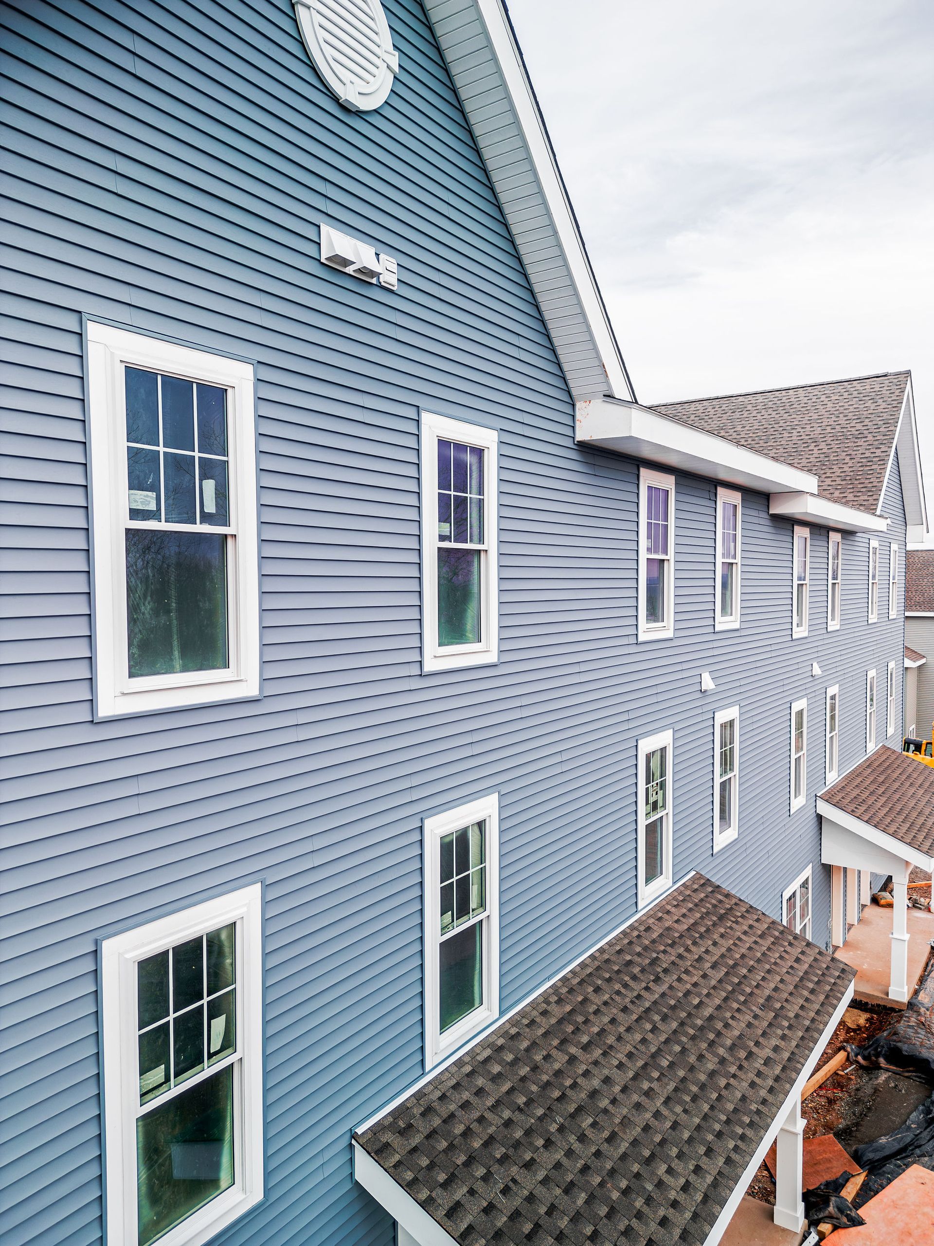 Blue sided multi-story building with white-framed windows, a brown roof, and a covered porch.