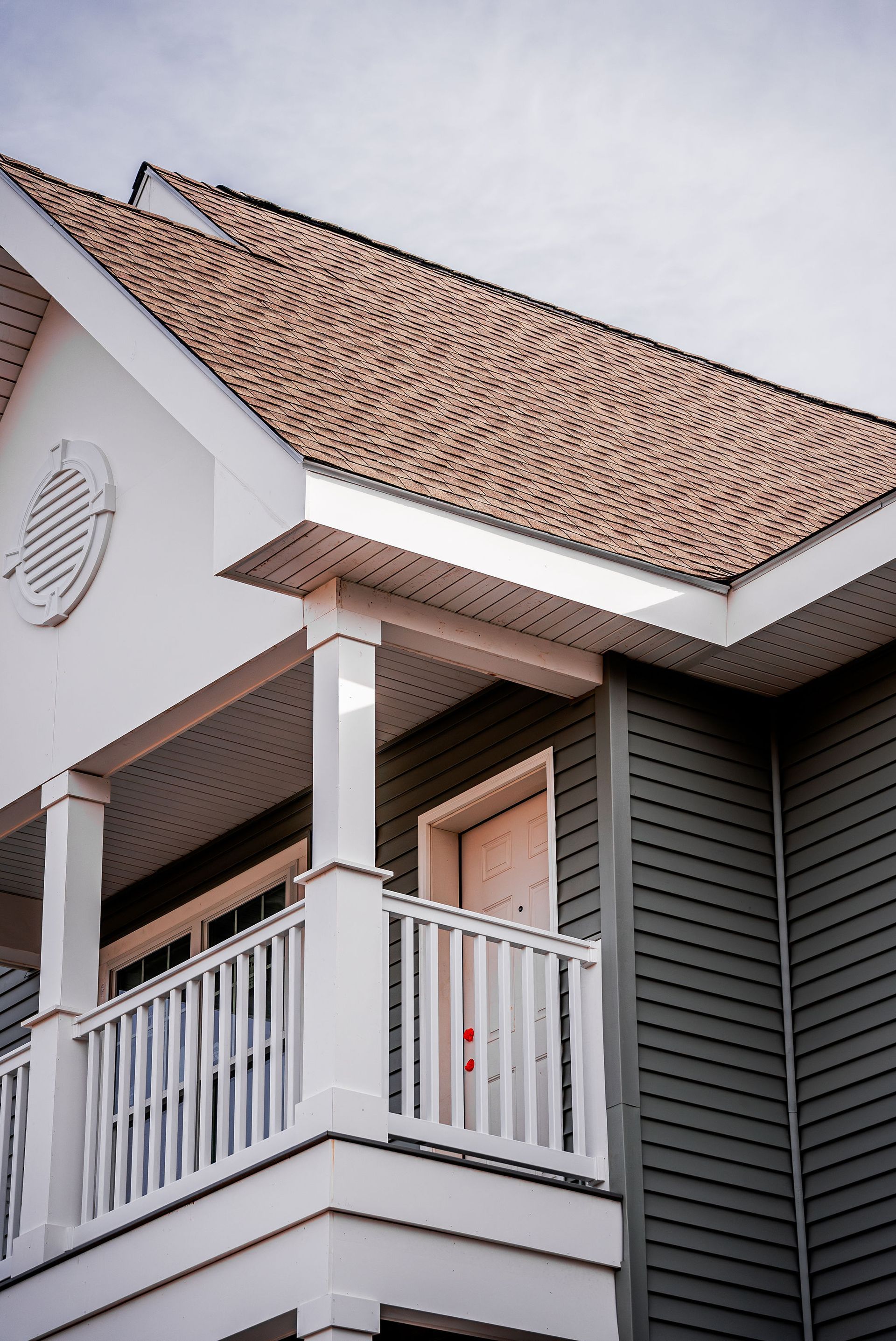 White porch with balustrade and green siding on a building. Brown roof.