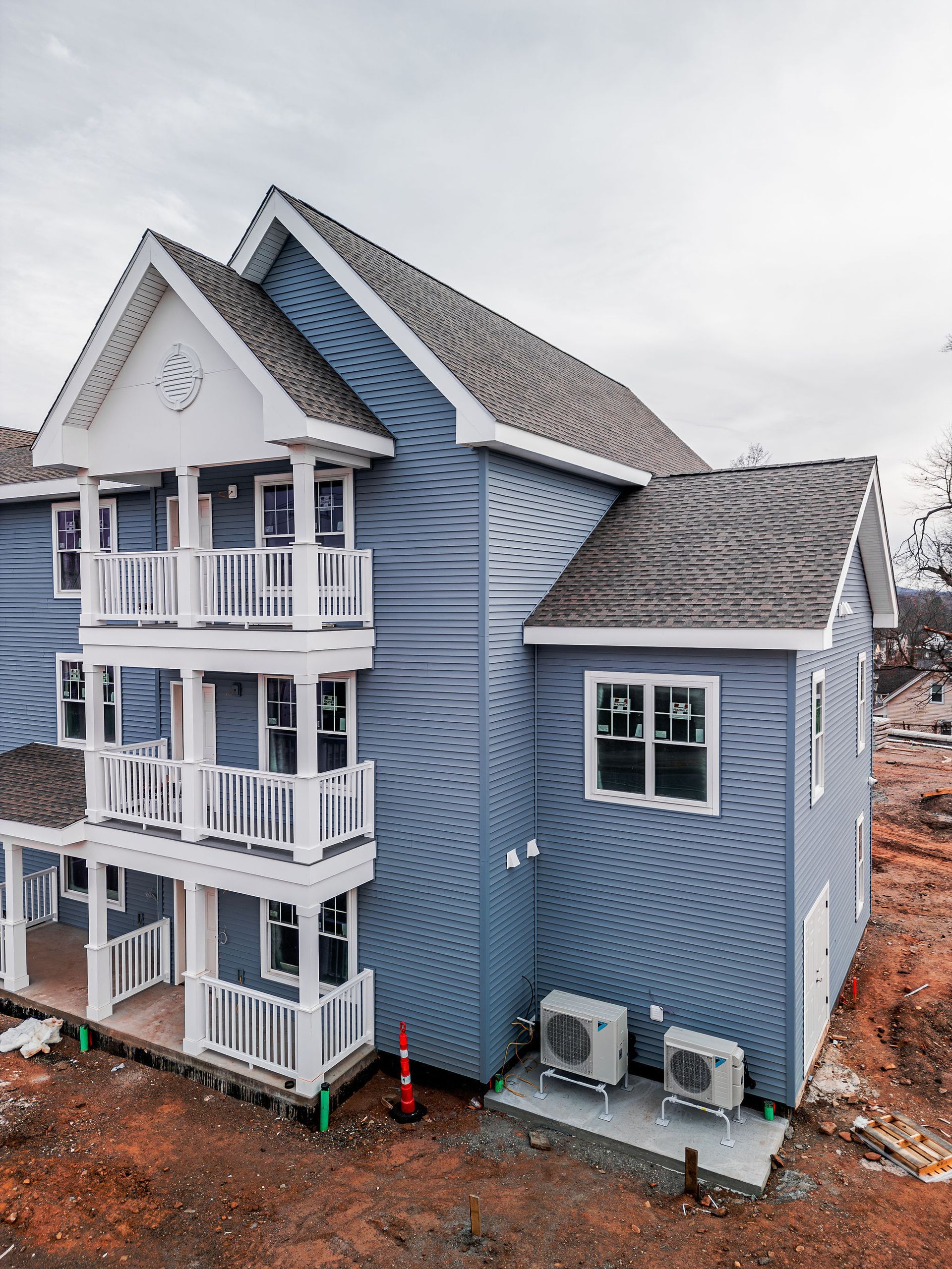 Three-story blue building with white balconies and trim, gray roof, and HVAC units outside.